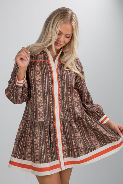 Woman wearing a patterned dress with orange trim on a plain background