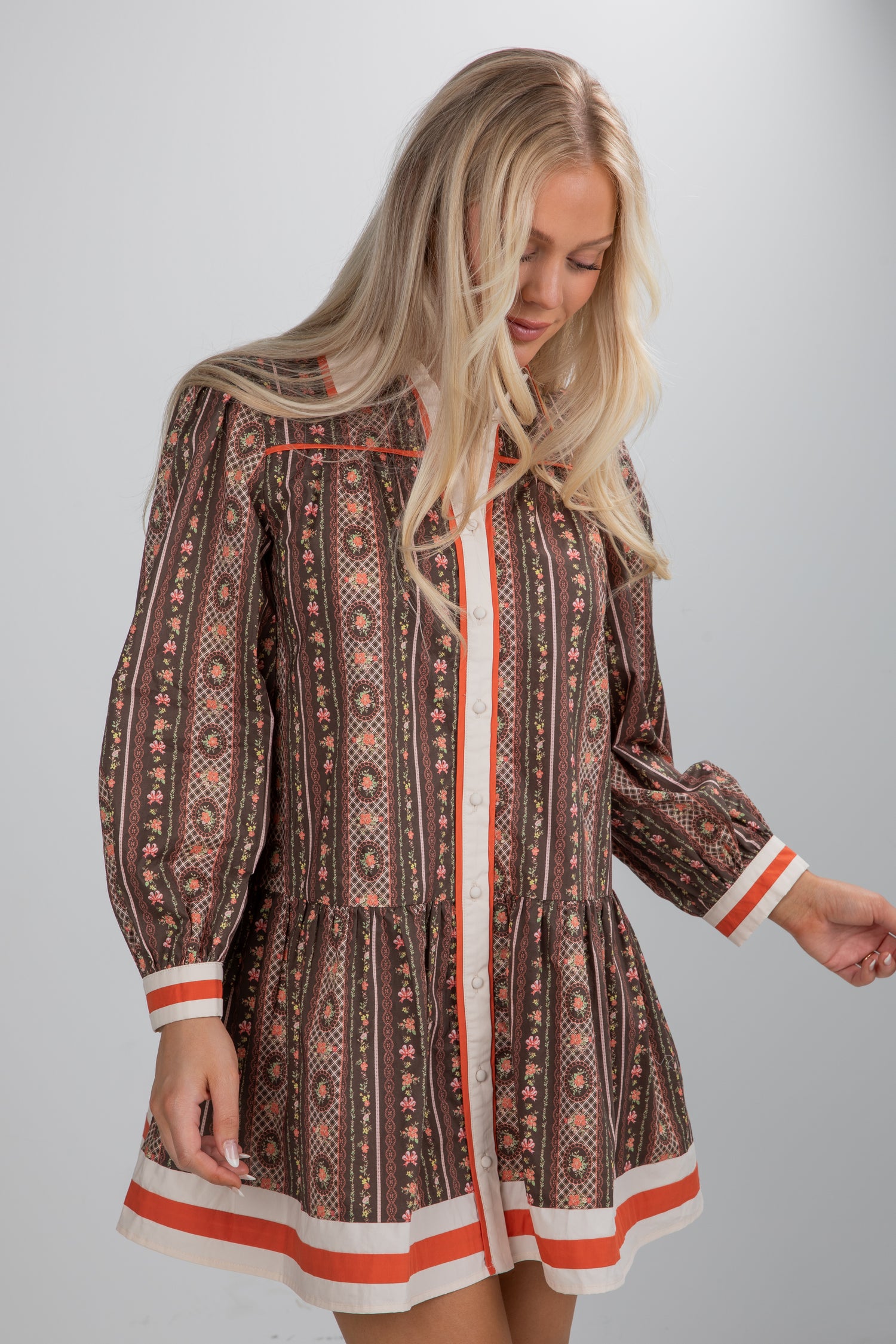 Woman wearing a patterned dress with long sleeves and trim on a plain background
