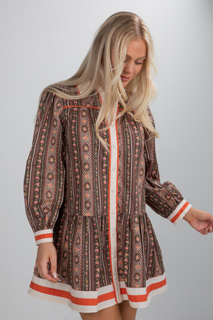 Woman wearing a patterned dress with long sleeves and trim on a plain background