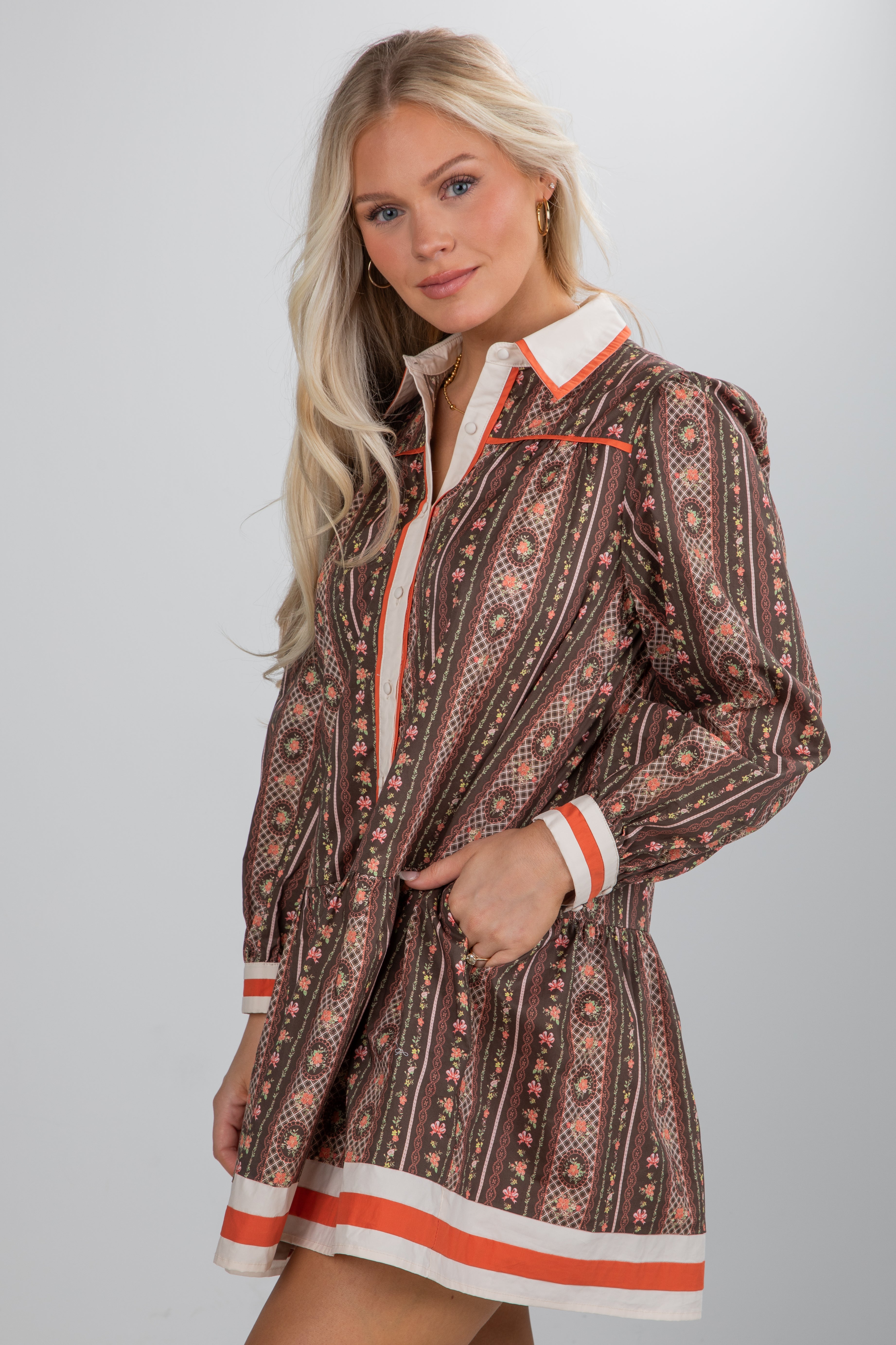 Woman wearing a patterned dress with orange and white accents on a plain background