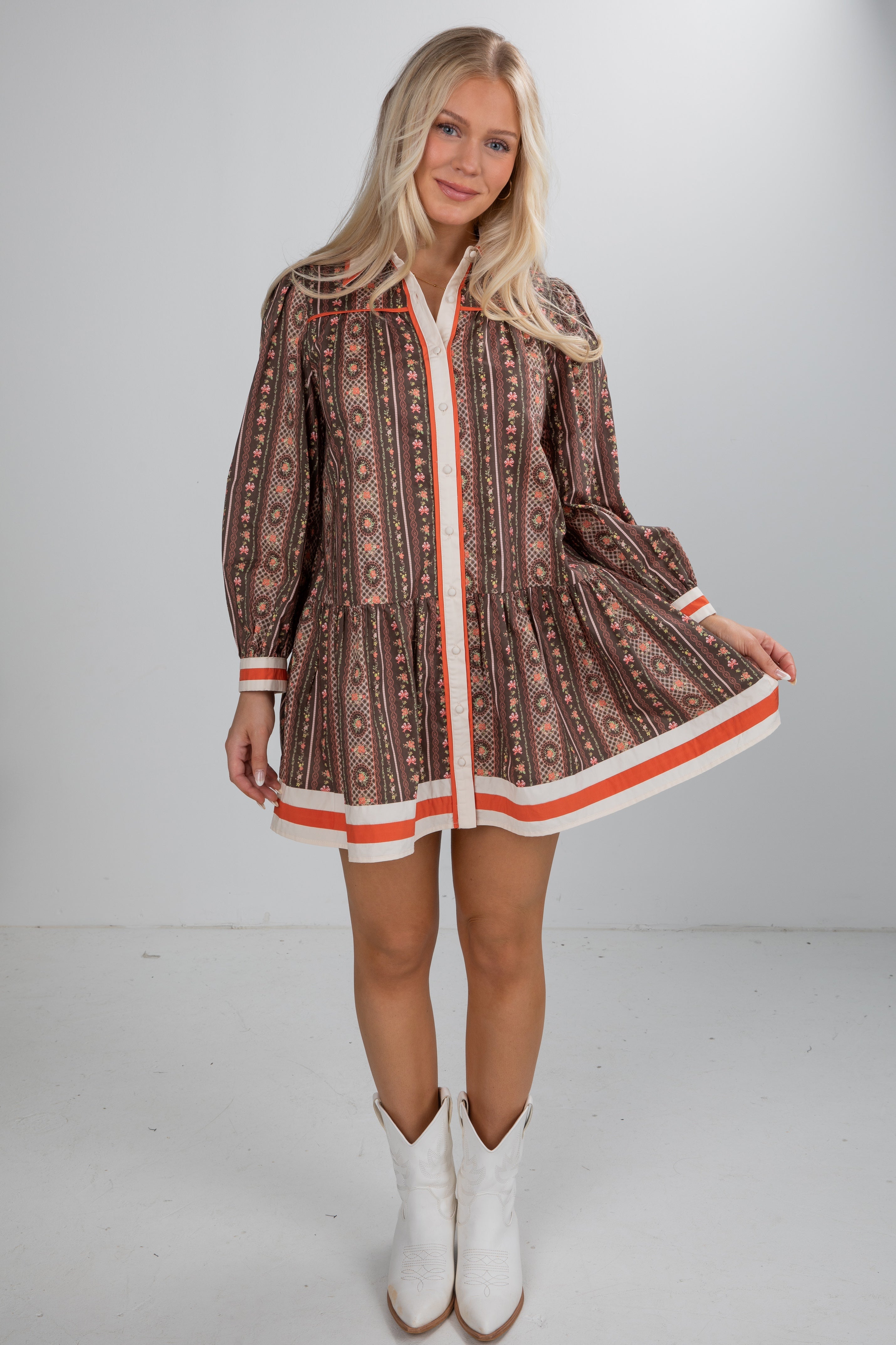 Woman wearing a patterned dress with long sleeves and white boots on a plain background