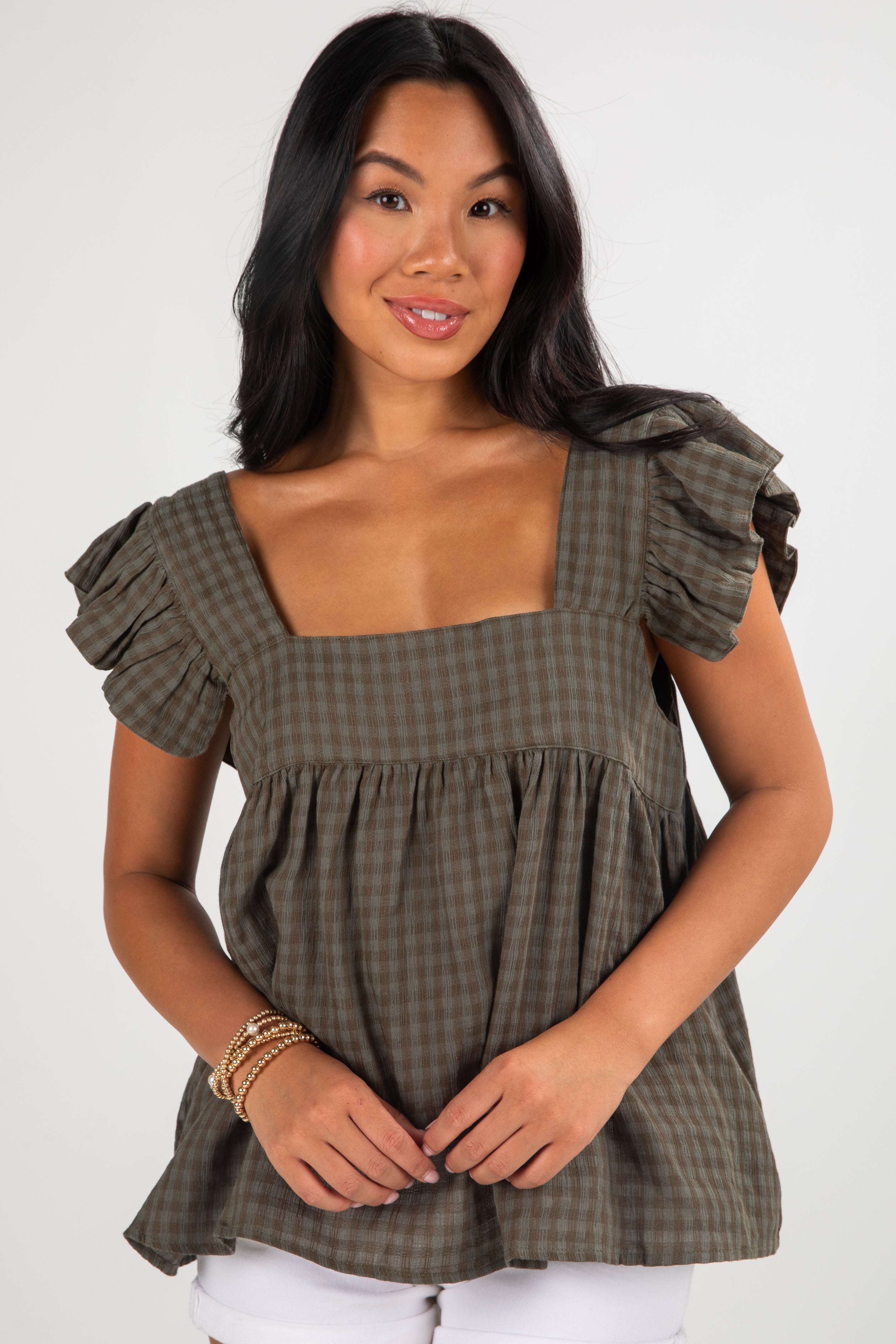 Woman wearing a green checkered top with ruffled sleeves on a white background