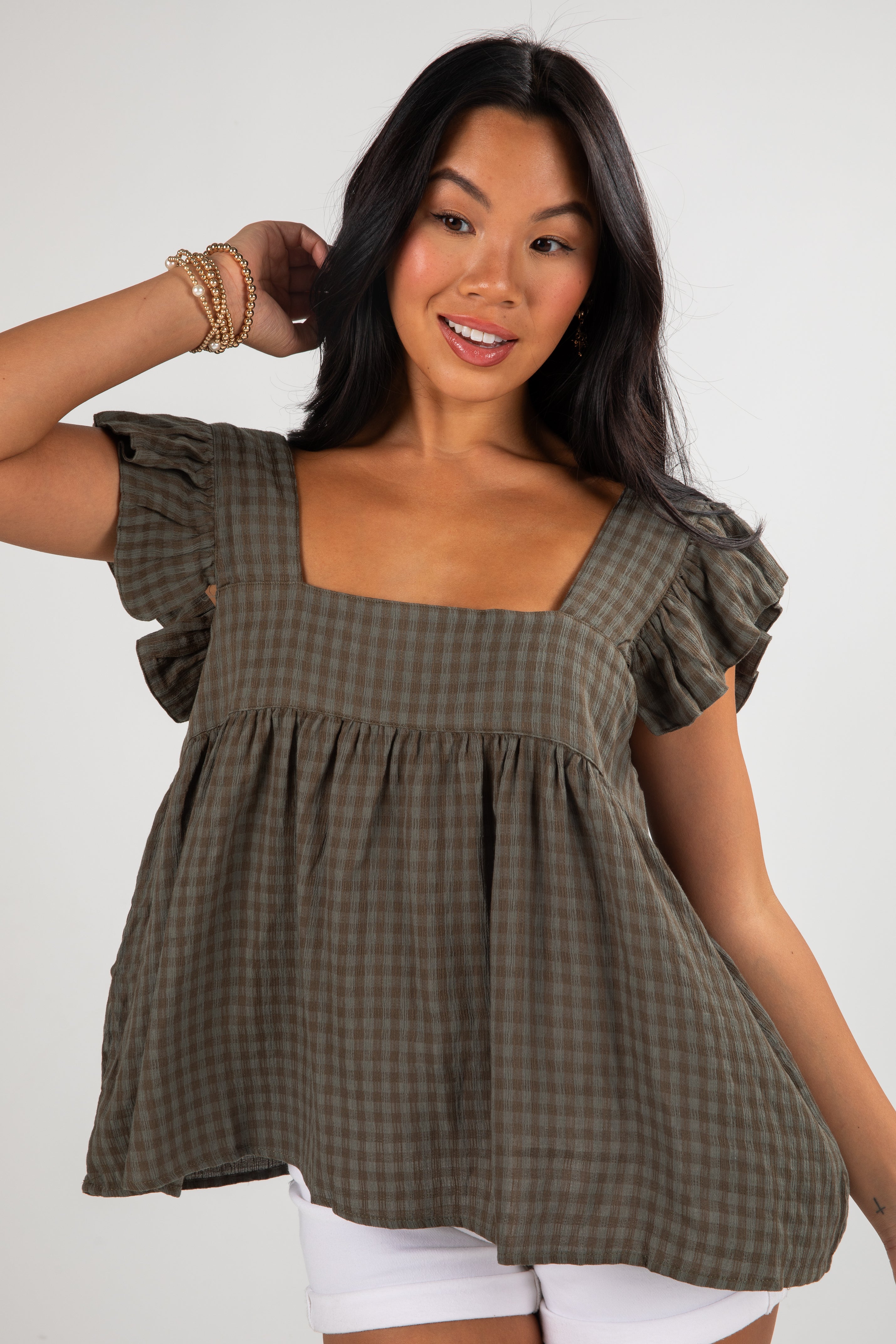 Woman wearing a green checkered top with ruffled sleeves on a white background