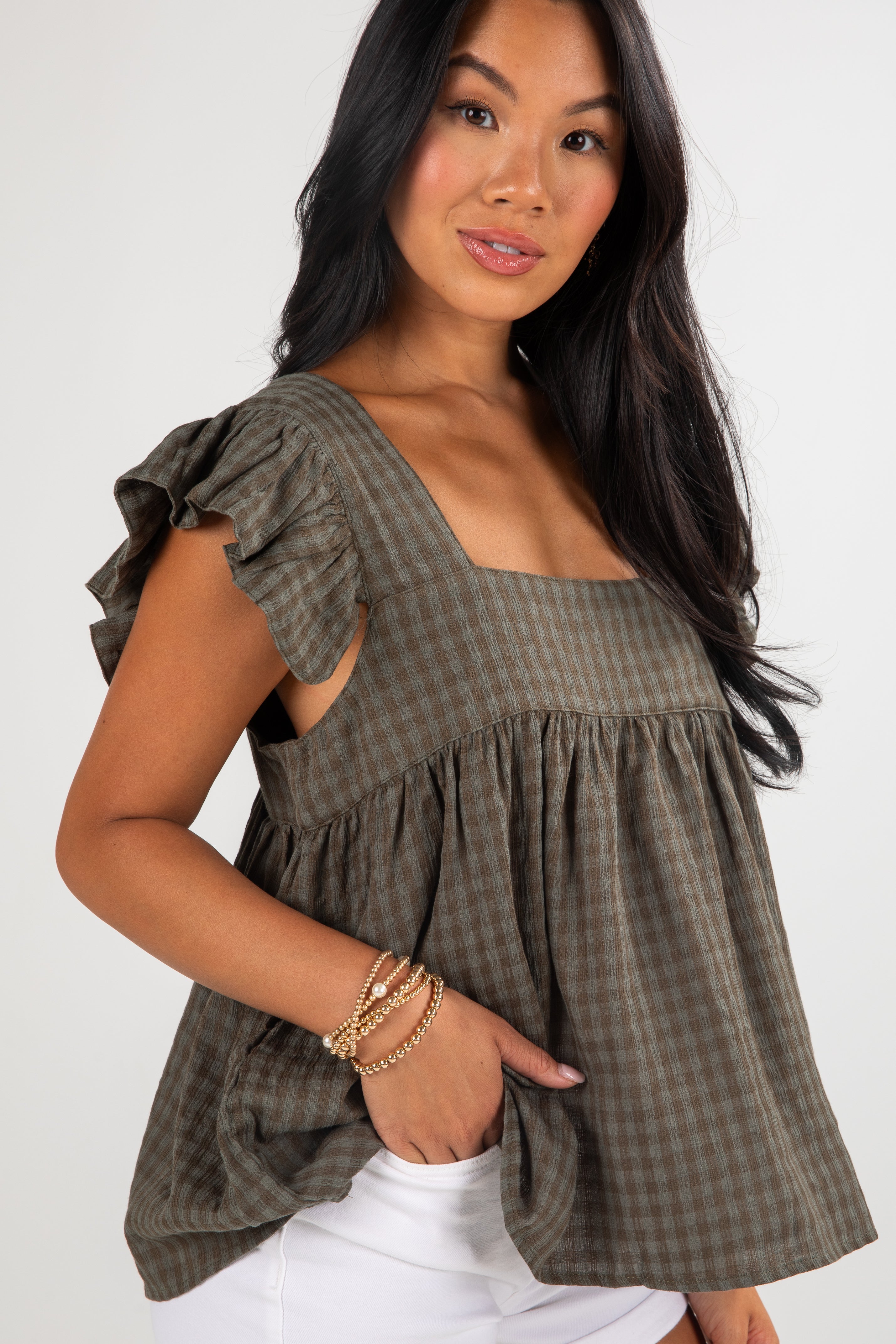 Woman wearing a green checkered top with ruffled sleeves on a white background