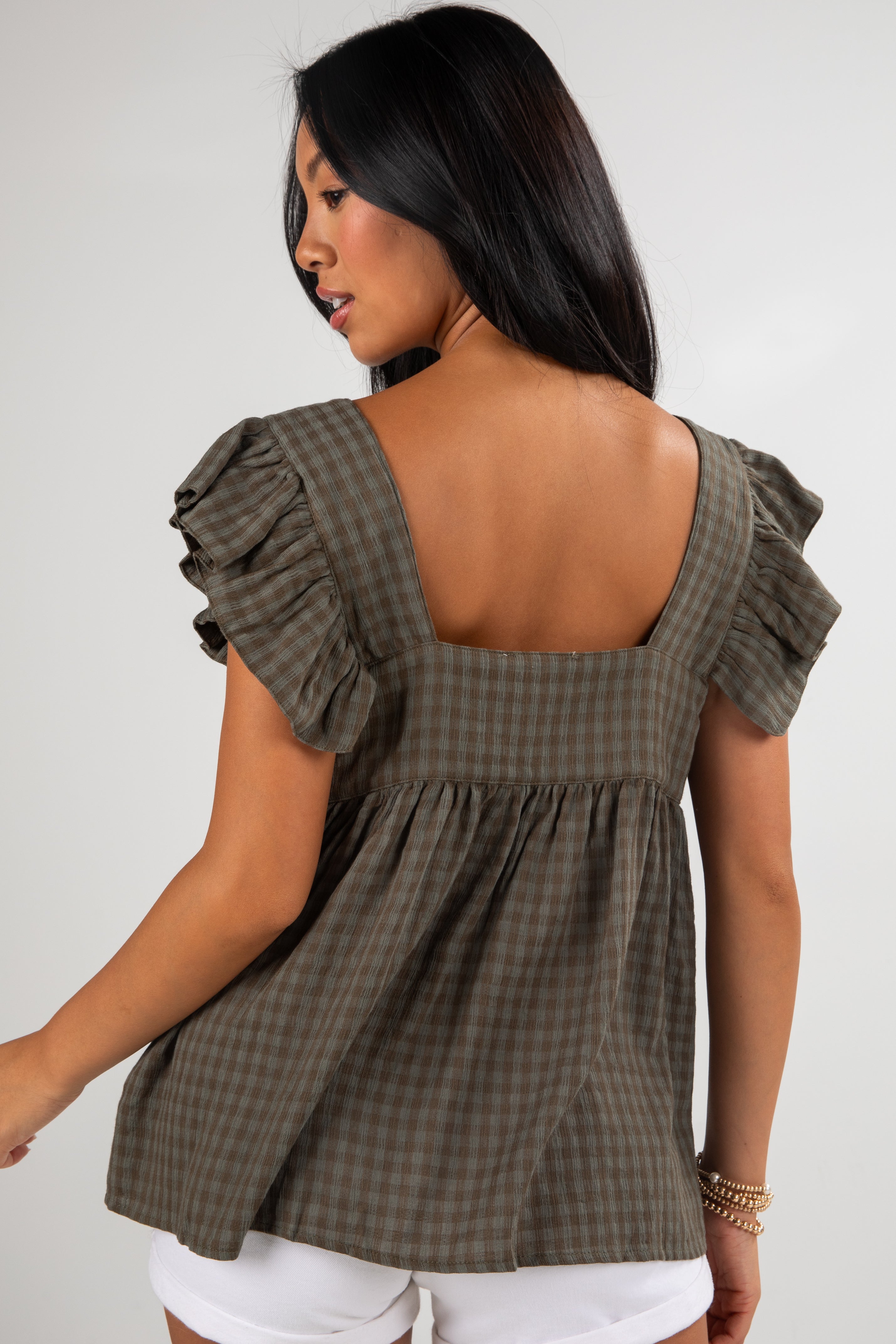 Woman wearing a green checkered top with ruffled sleeves on a plain background