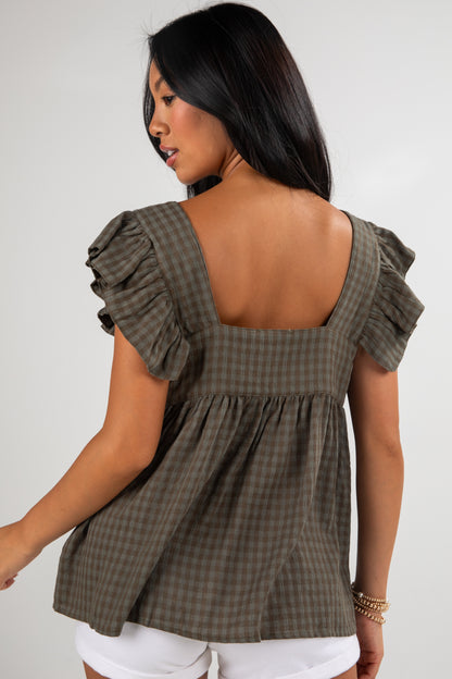 Woman wearing a green checkered top with ruffled sleeves on a plain background