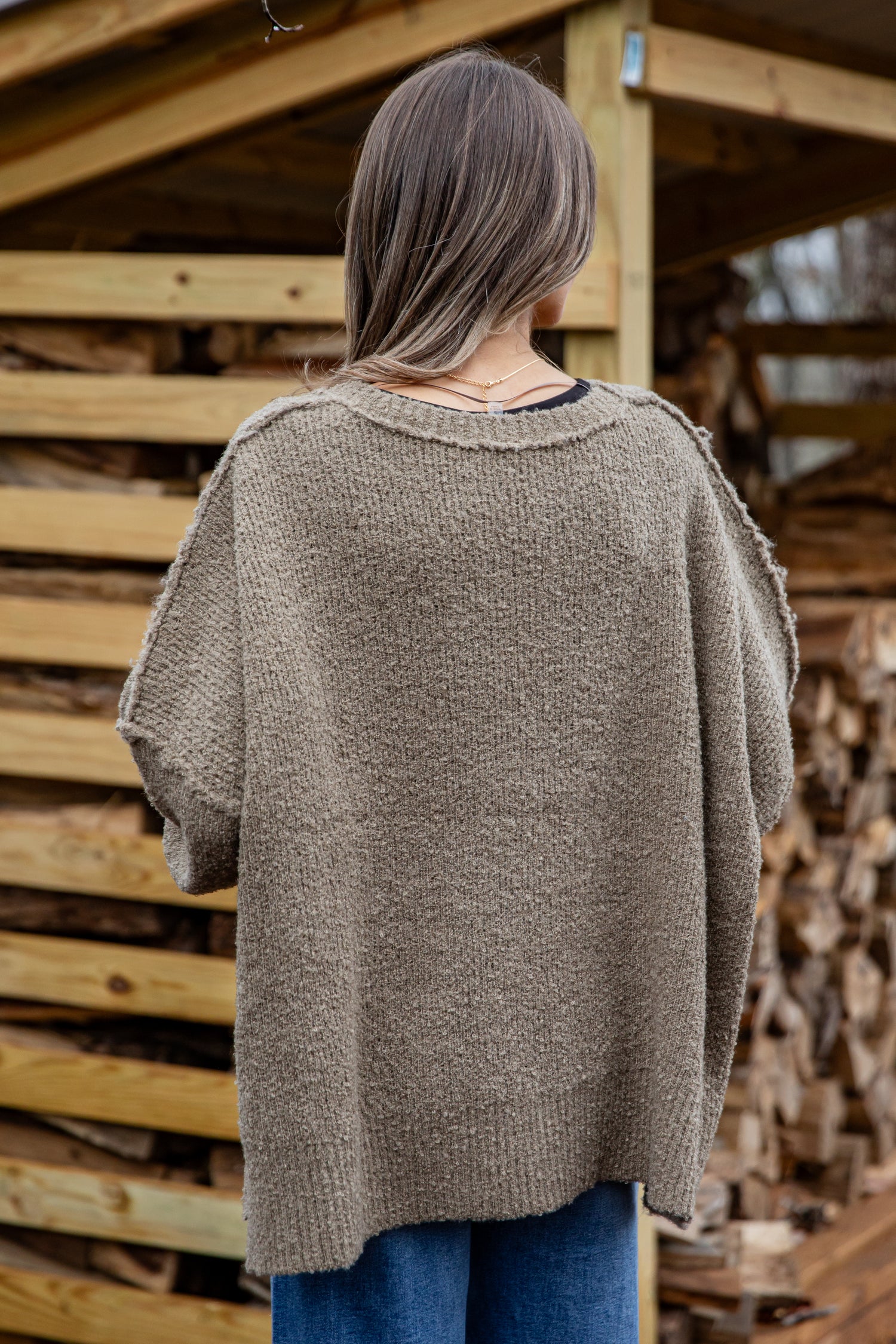 Person wearing a brown poncho standing in front of stacked firewood.