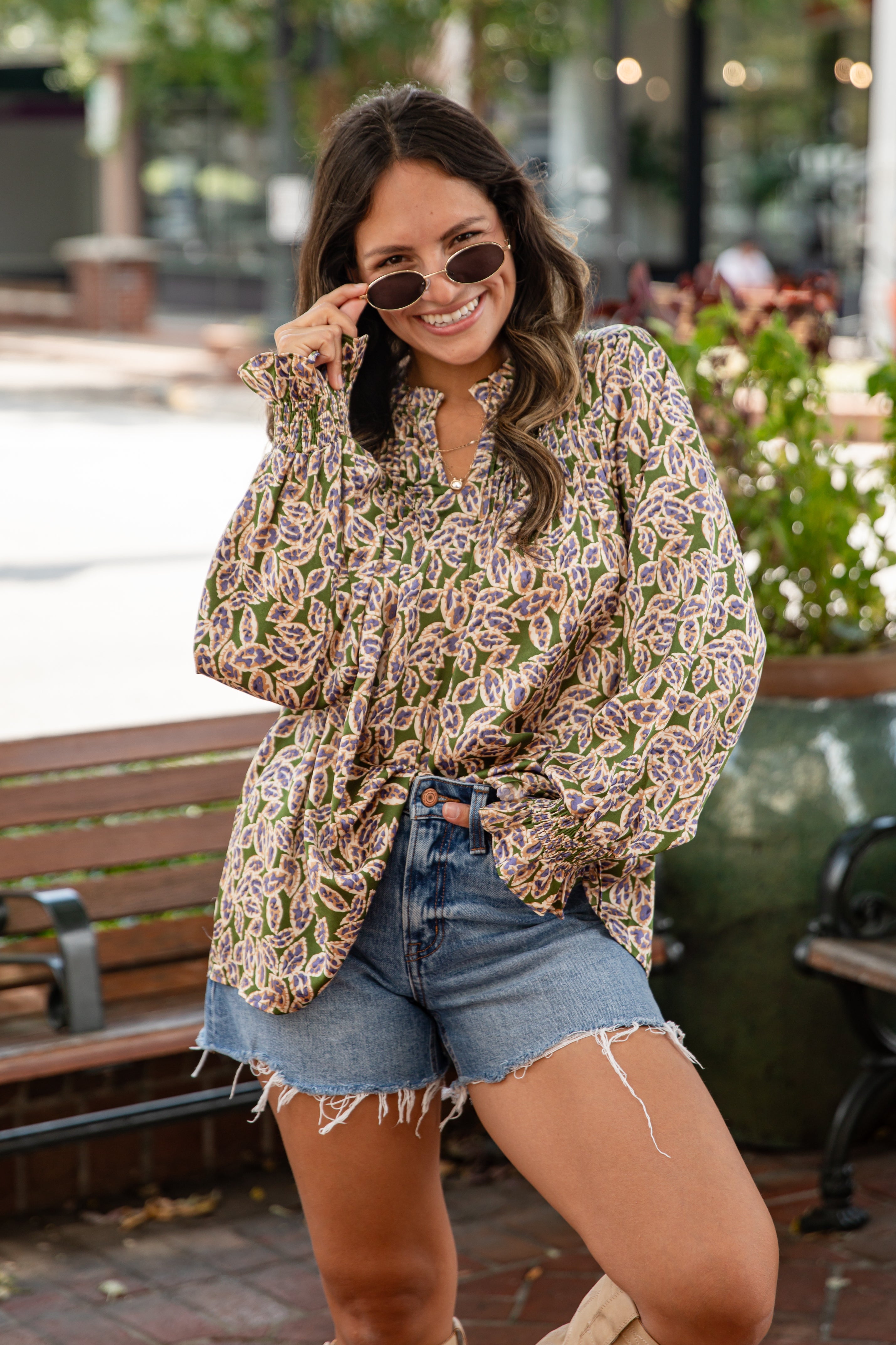 Woman wearing a patterned blouse and denim shorts outdoors.