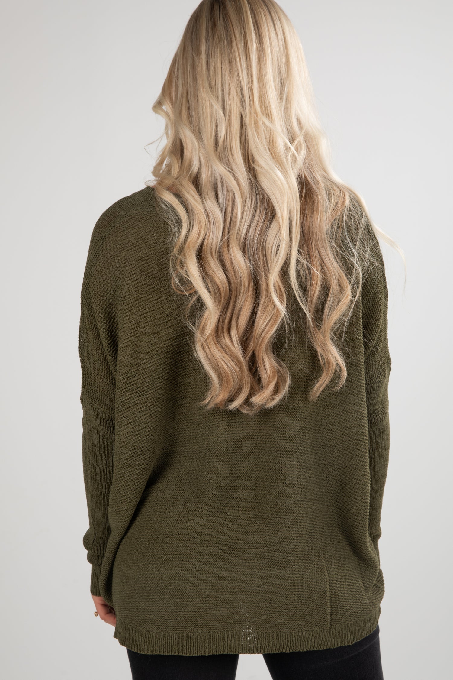 Person wearing a green sweater with long blonde hair on a white background