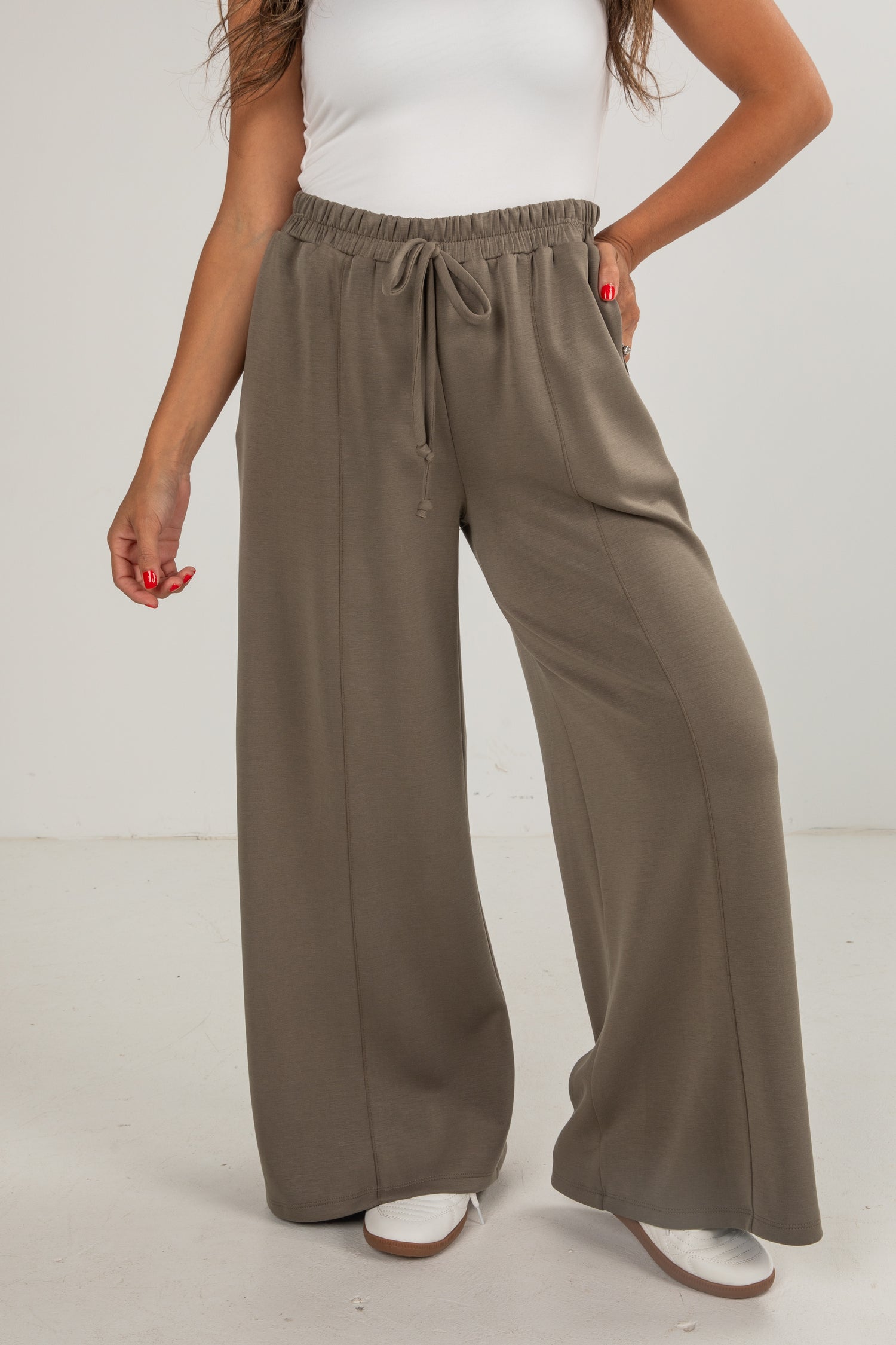 Person wearing brown wide-leg pants and a white top on a plain background