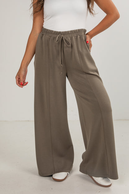 Person wearing brown wide-leg pants and a white top on a plain background