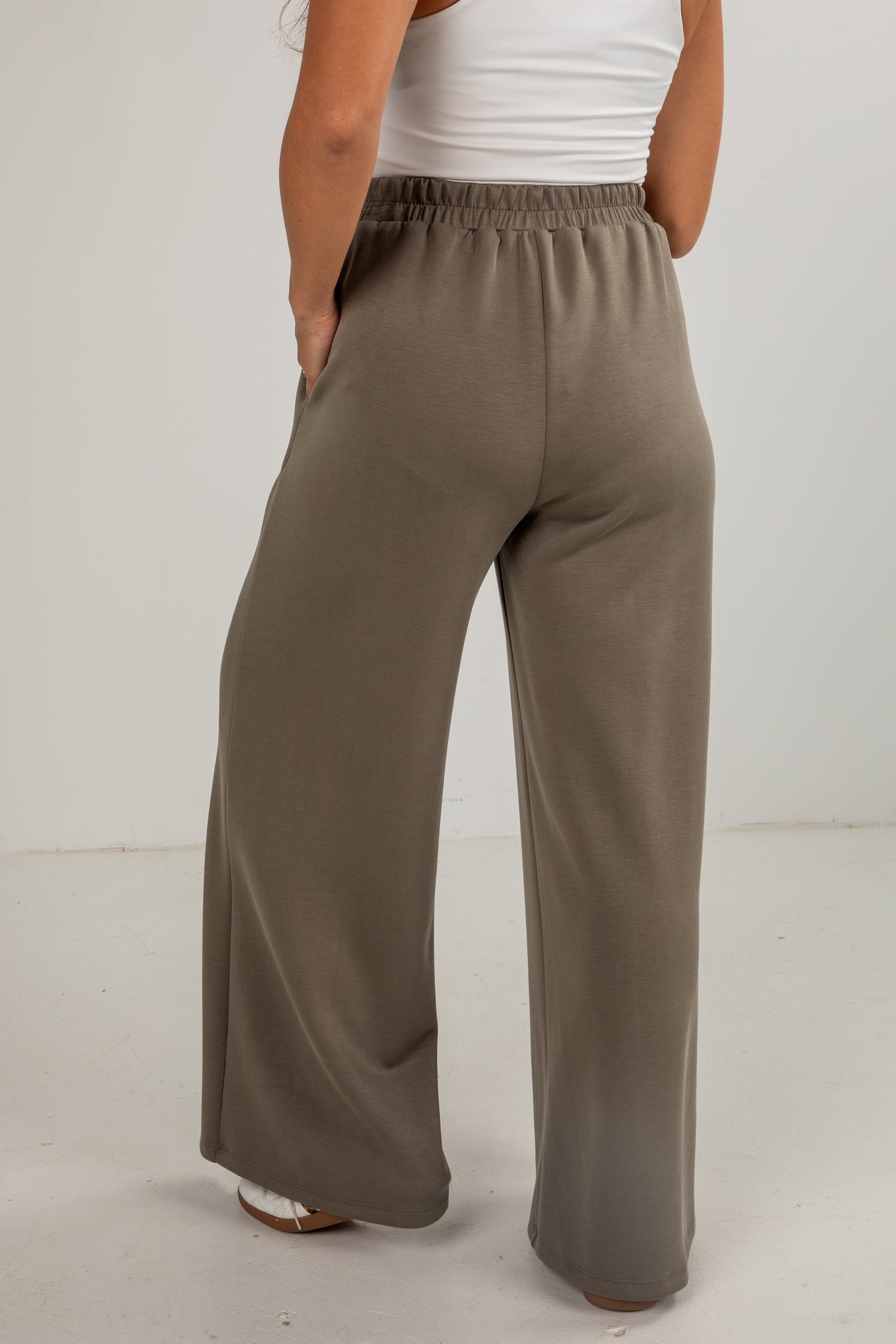 Person wearing brown wide-leg pants and a white top on a plain background
