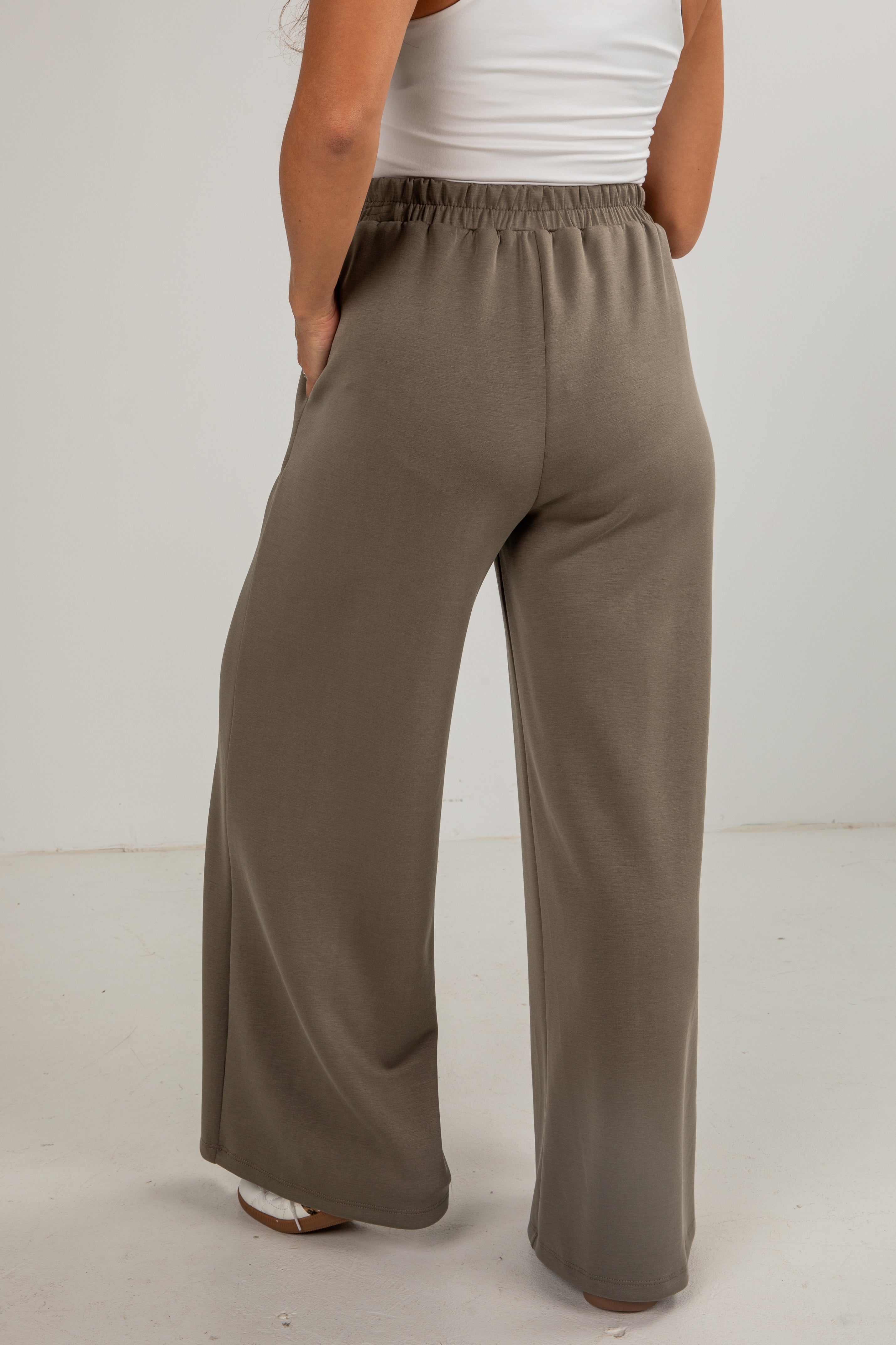 Person wearing brown wide-leg pants and a white top on a plain background