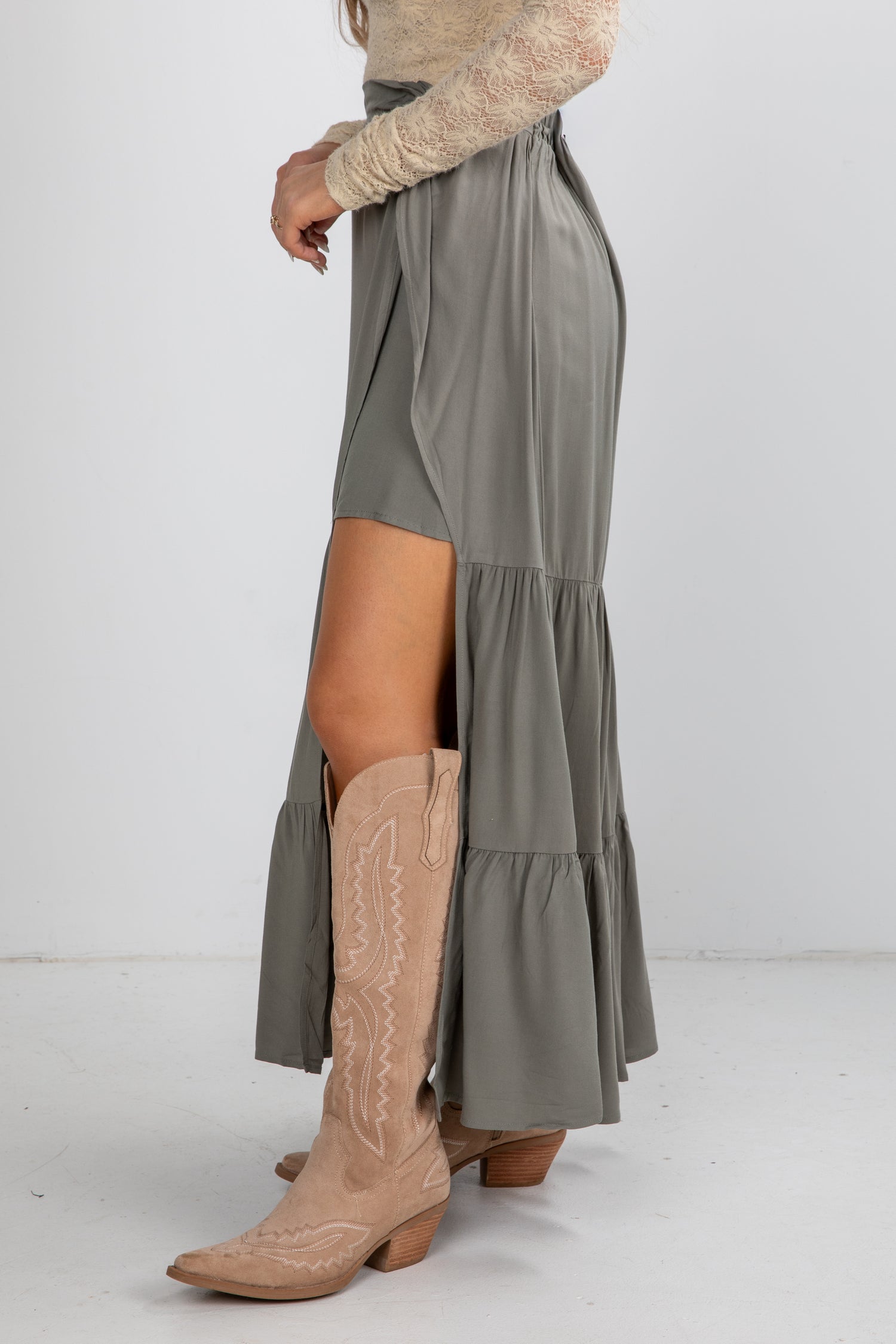 Person wearing a long gray skirt with a high slit and beige cowboy boots on a white background