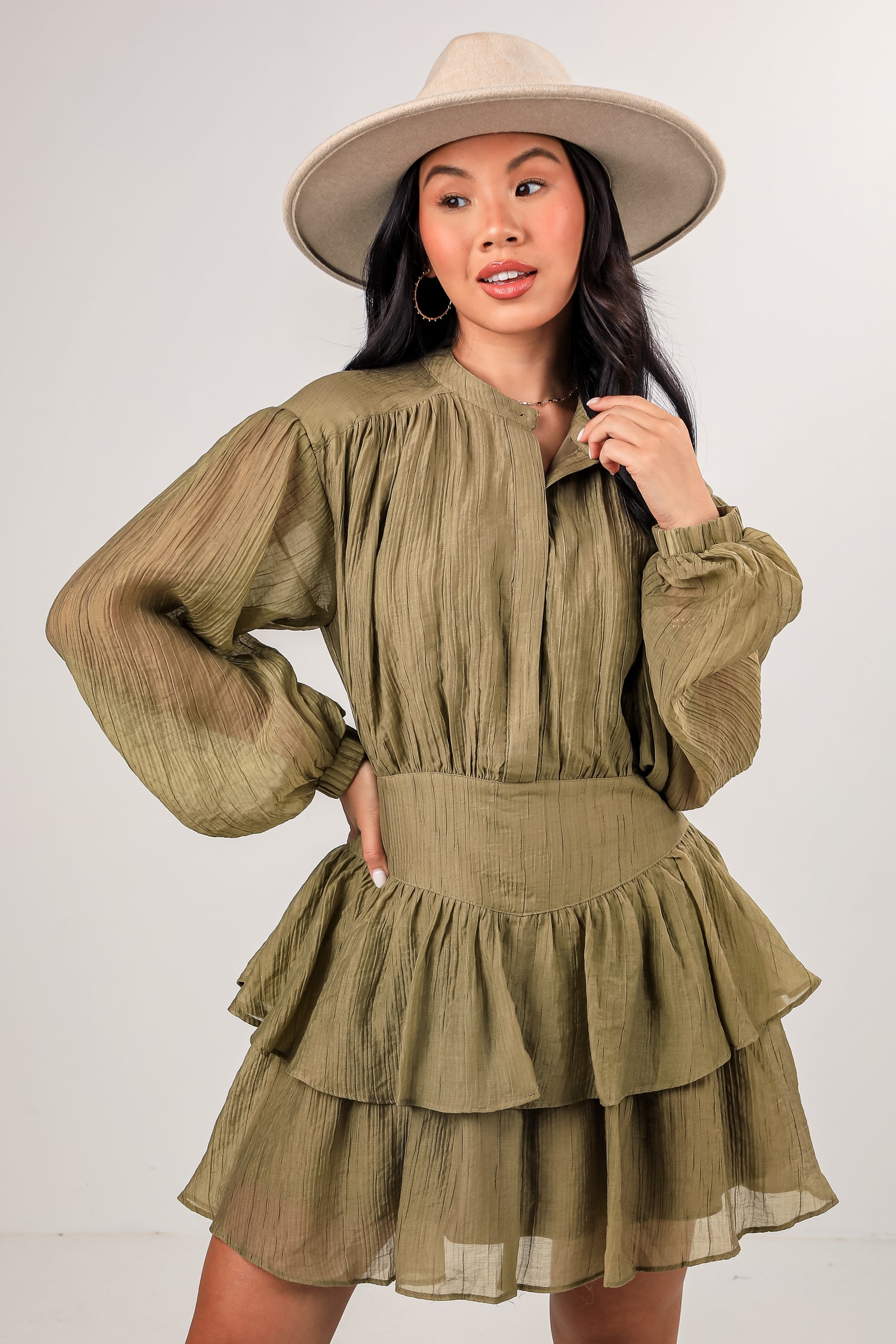 Woman wearing a green dress with long sleeves and a hat on a white background