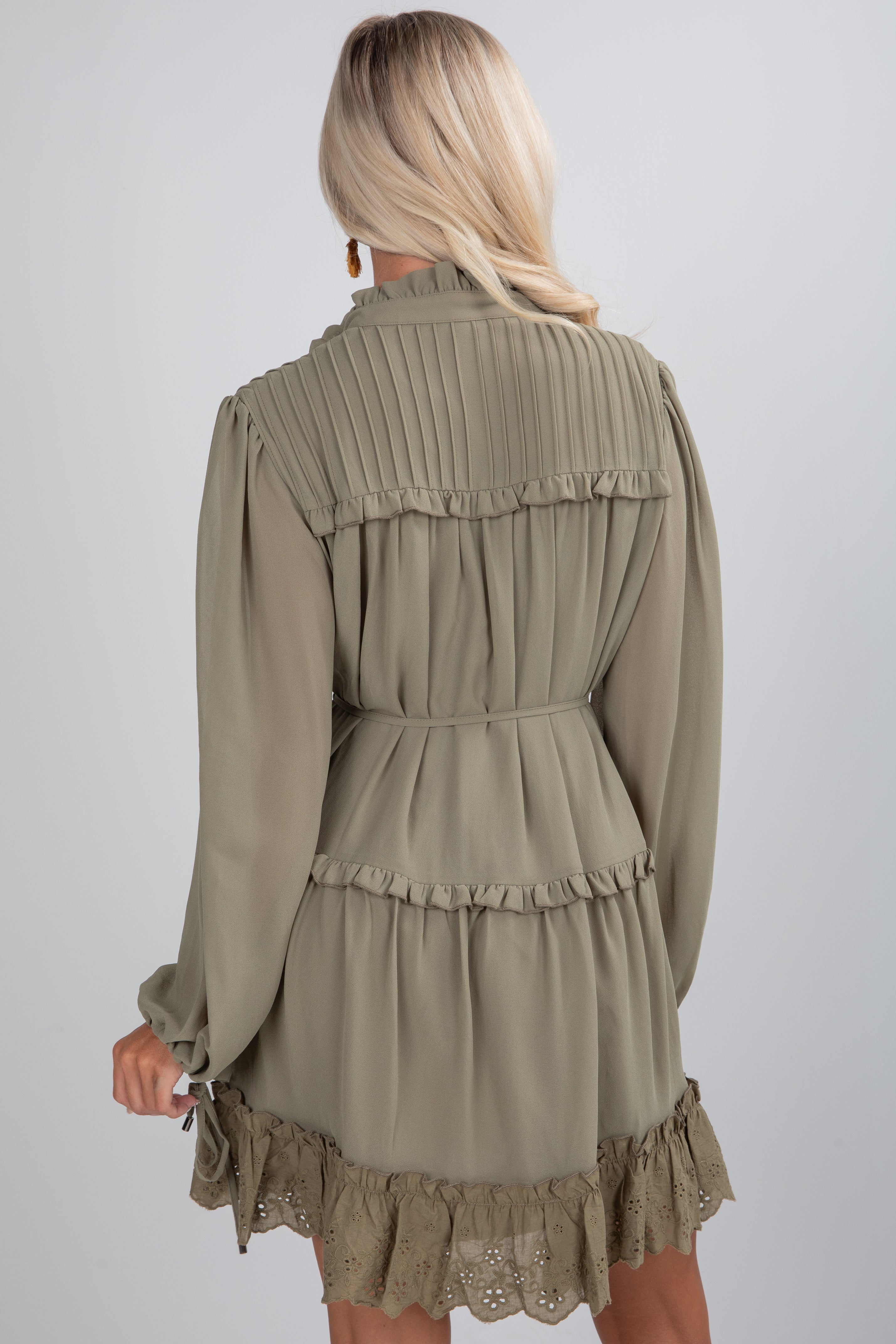 Woman wearing a beige dress with long sleeves and ruffled details on a plain background