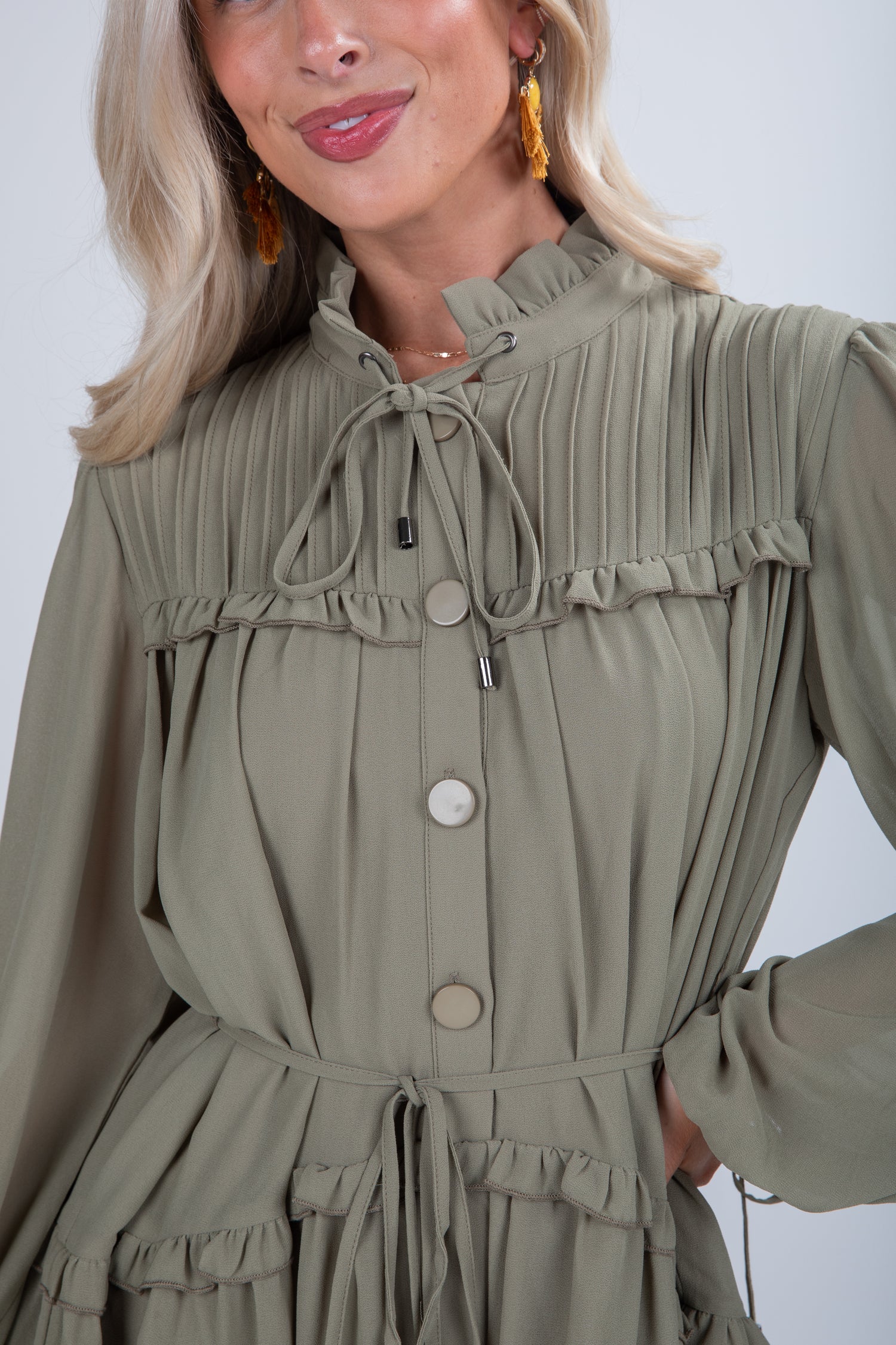 Woman wearing a green dress with long sleeves and buttons on a white background