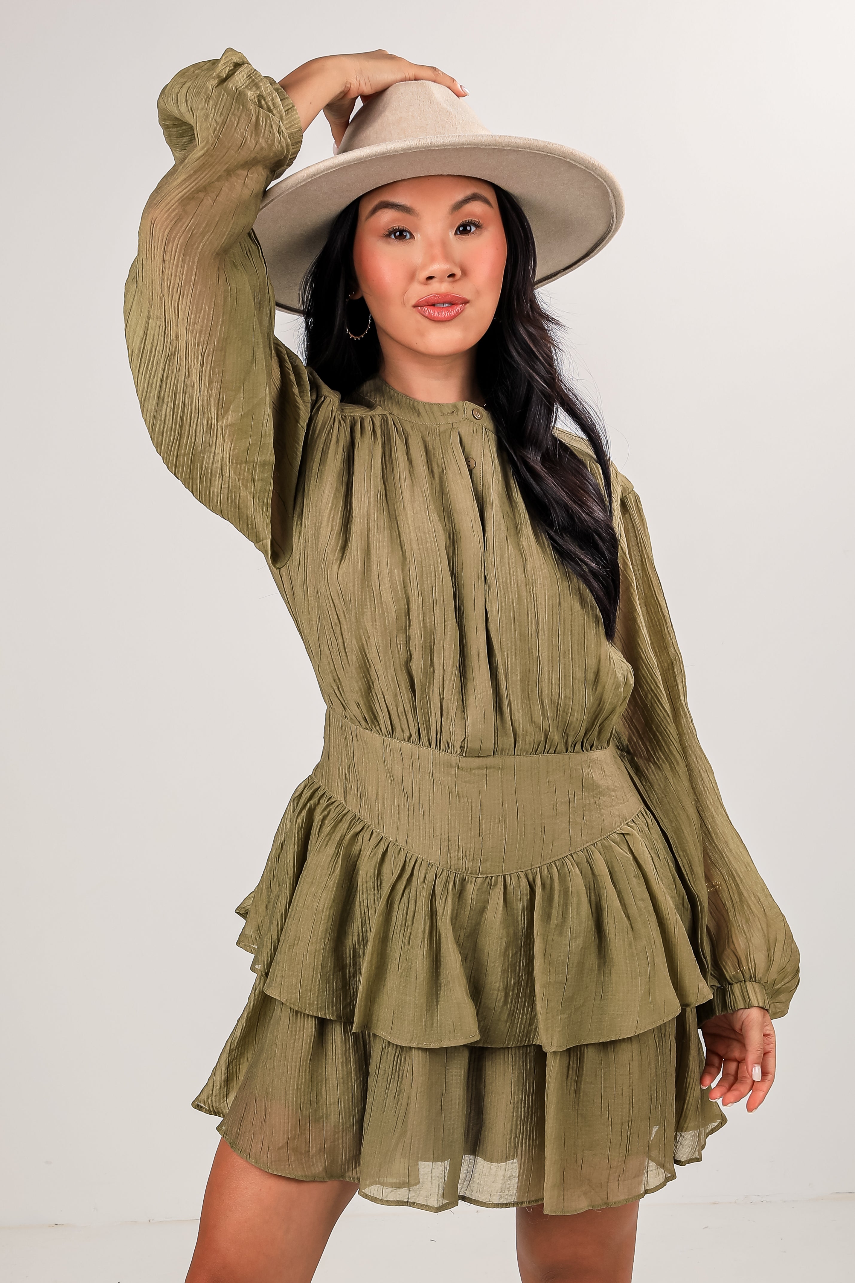 Woman wearing a green dress with ruffled layers and a beige hat on a white background