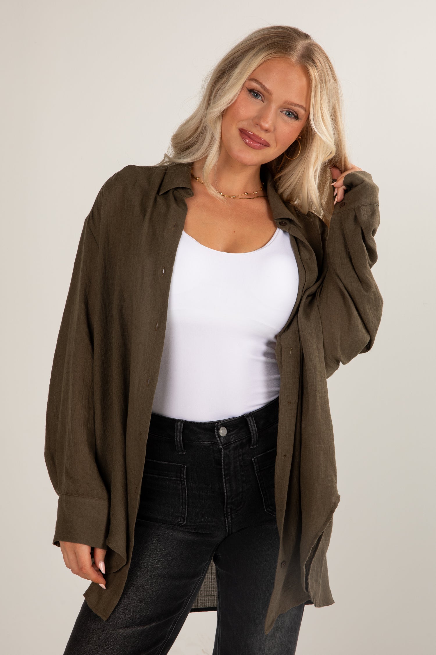 Woman wearing a green shirt over a white top and black pants on a plain background