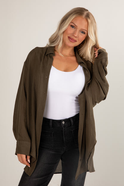 Woman wearing a green shirt over a white top and black pants on a plain background