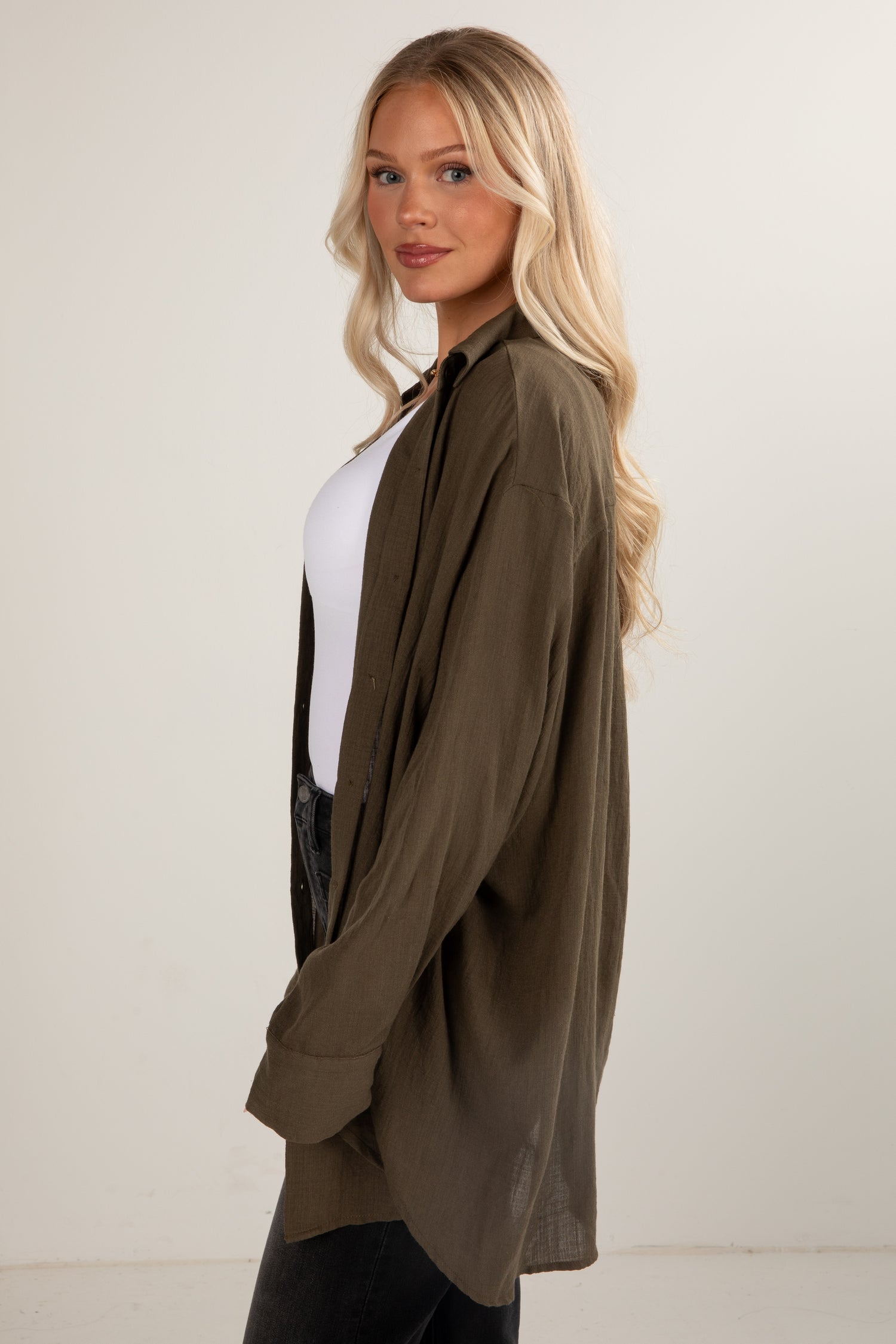 Woman wearing an olive green cardigan over a white shirt and black pants on a plain background
