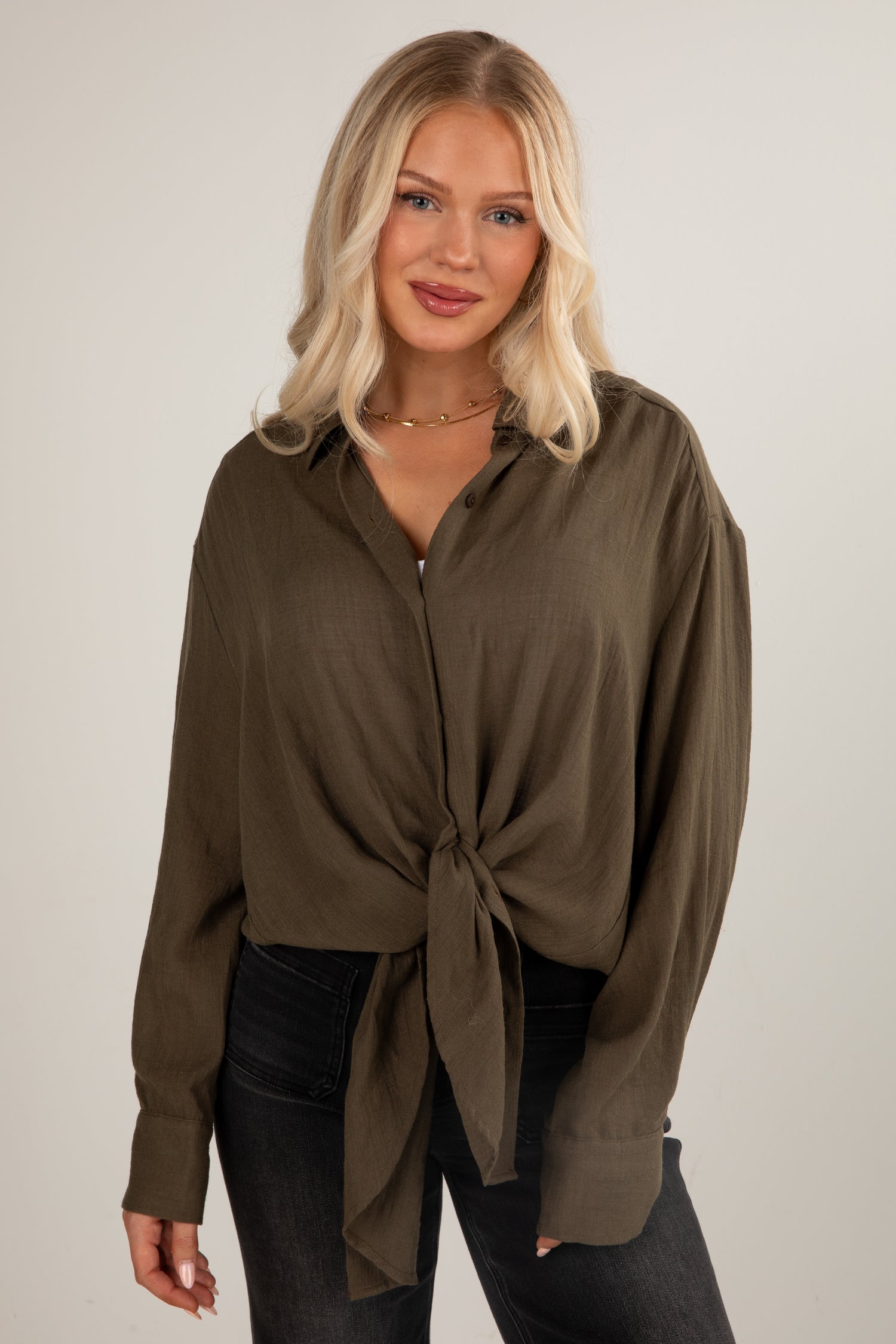 Woman wearing a brown button-up shirt with a tie detail against a plain background