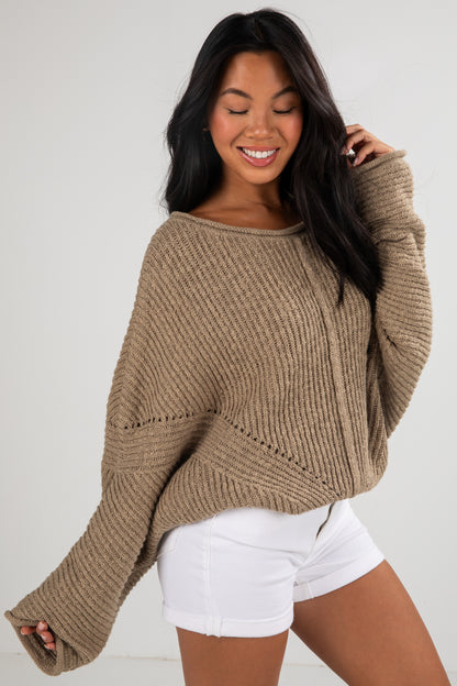 Woman wearing a brown sweater and white shorts against a plain background