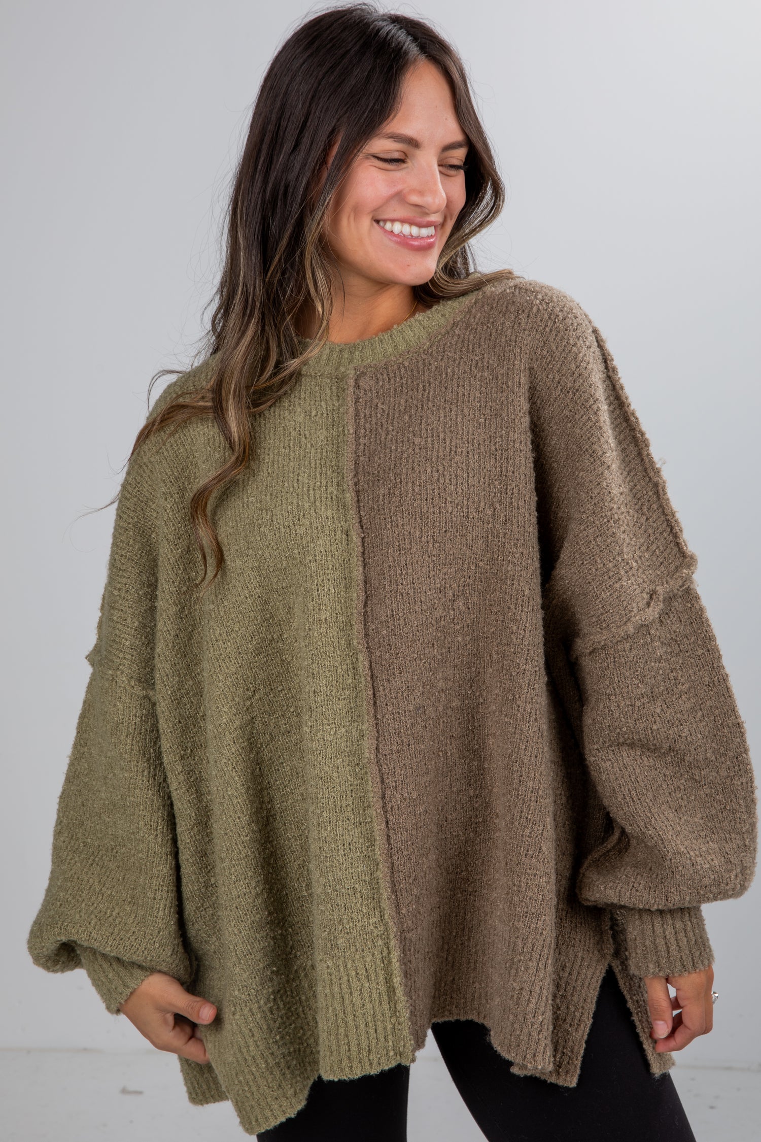 Woman wearing a two-tone sweater with green and brown sections on a plain background