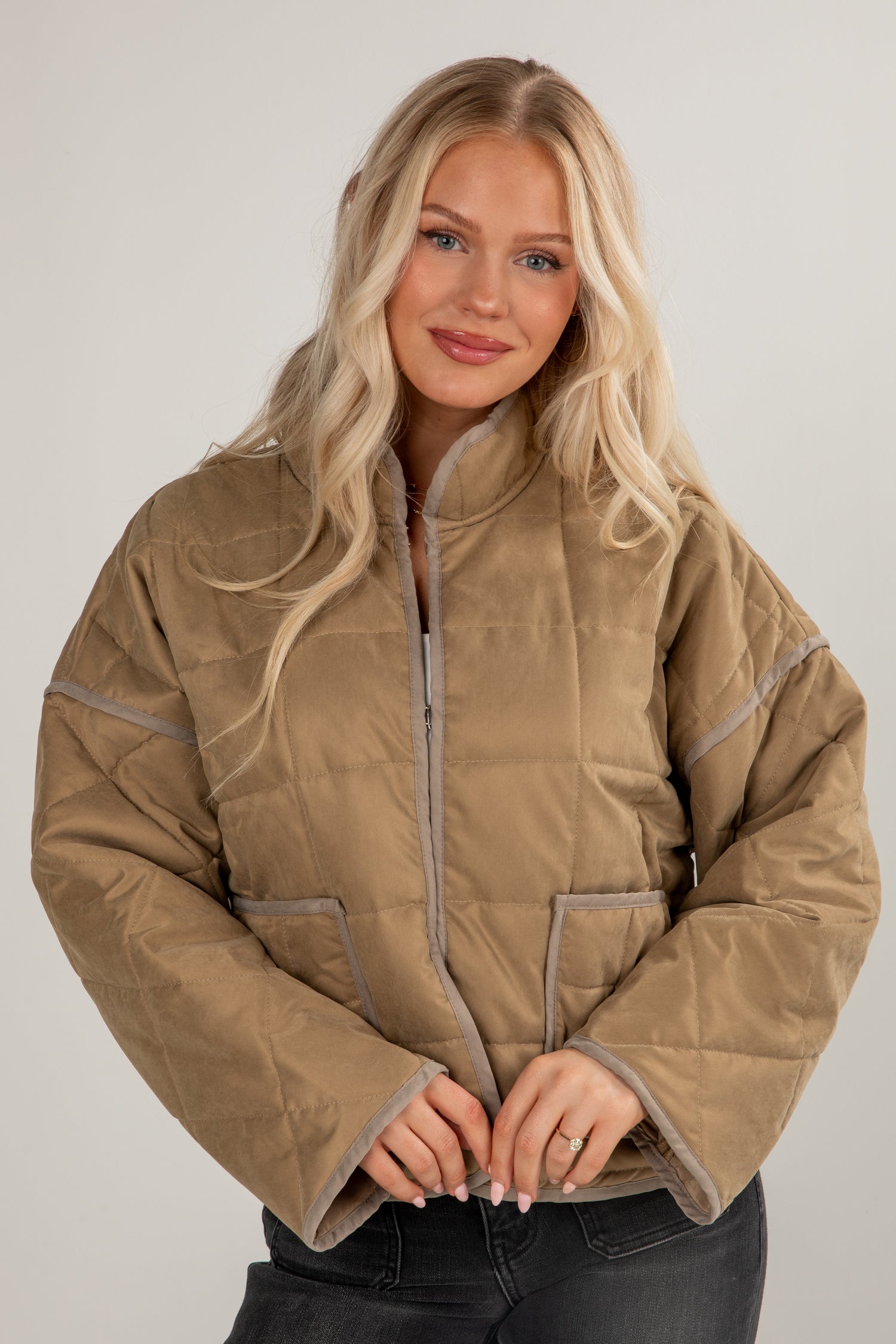 Woman wearing a beige quilted jacket against a plain background