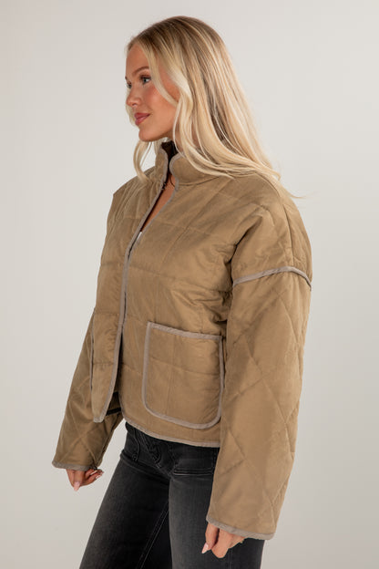 Woman wearing a beige quilted jacket on a plain background