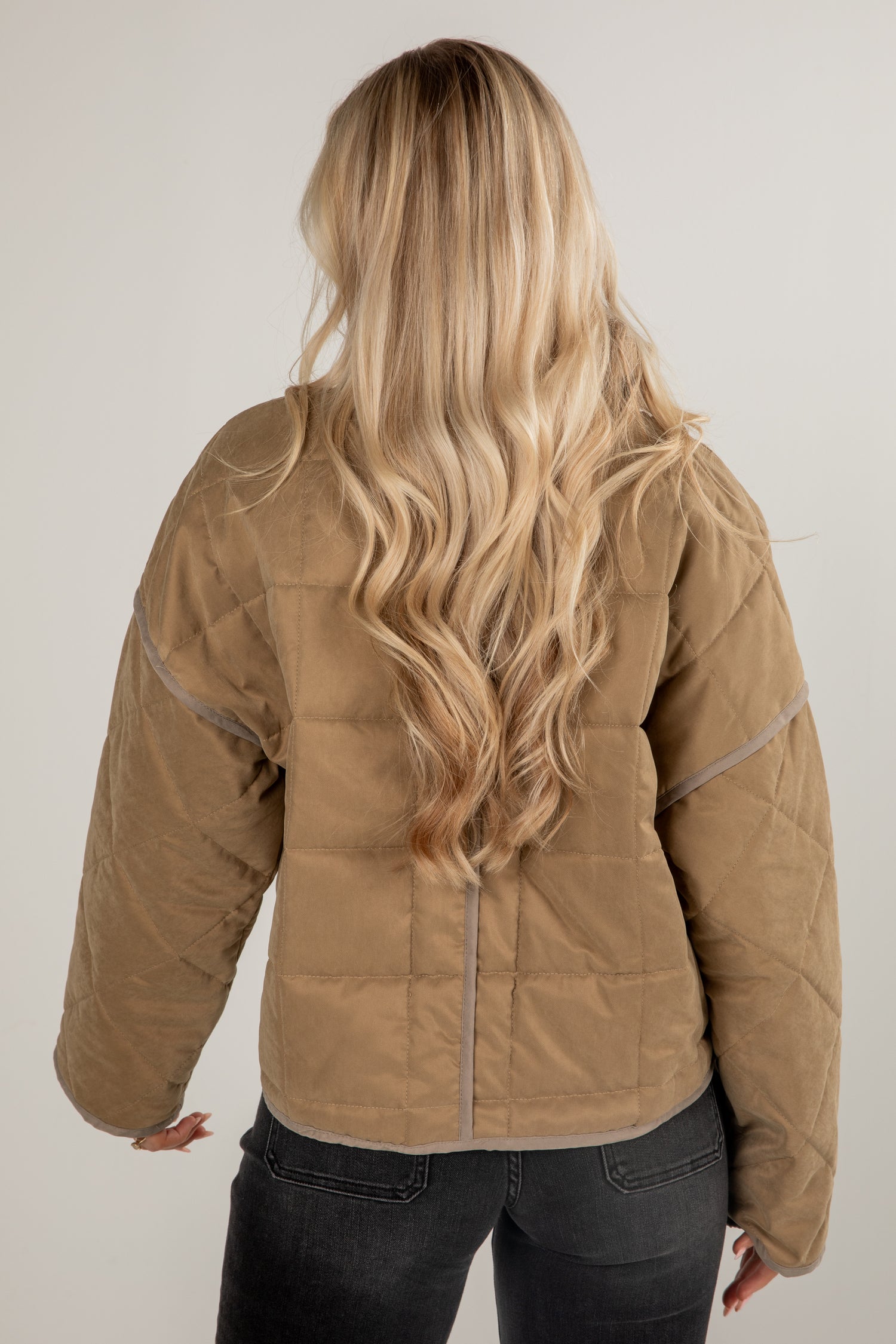 Person wearing a brown quilted jacket with long blonde hair on a plain background