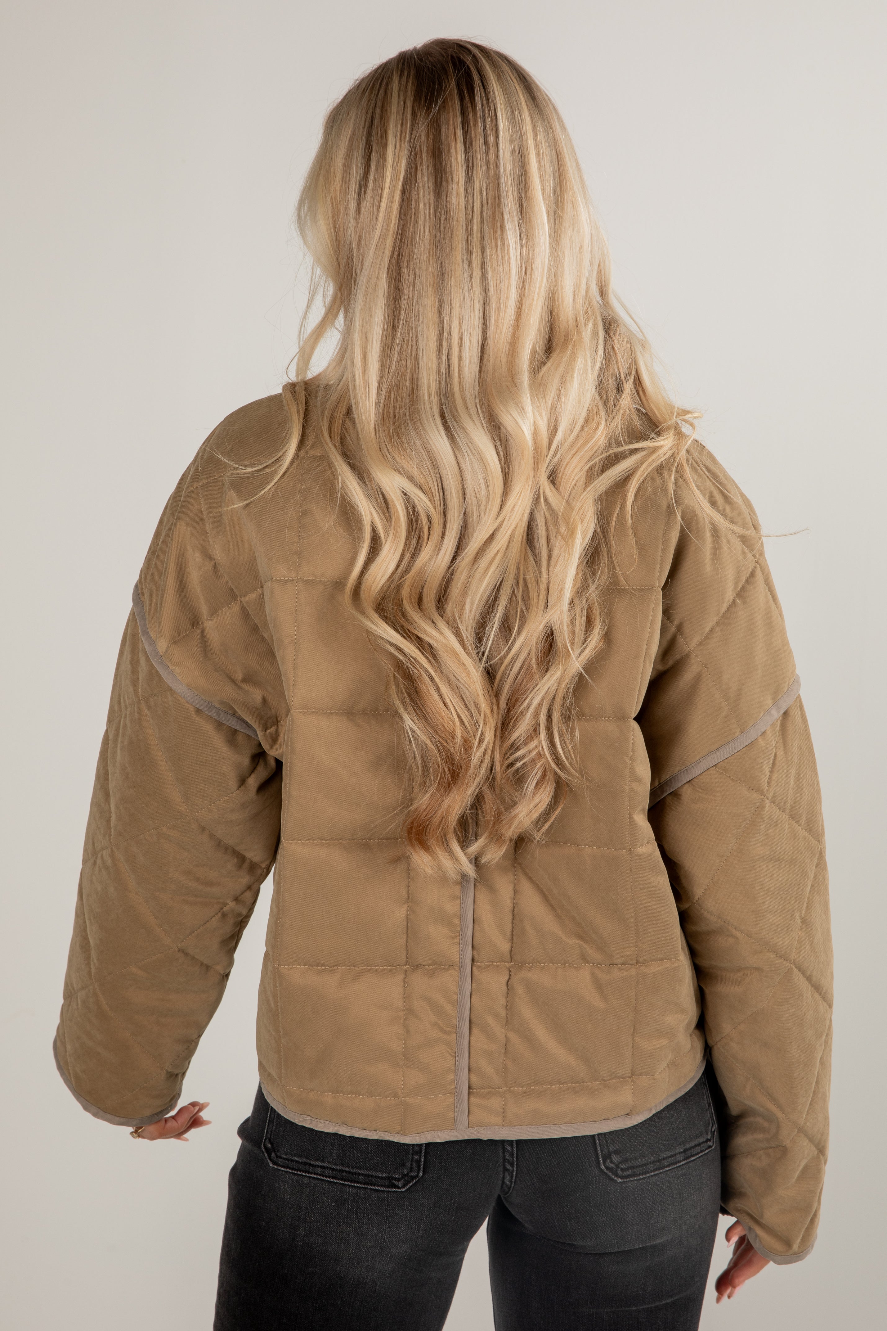 Person wearing a brown quilted jacket with long blonde hair on a plain background