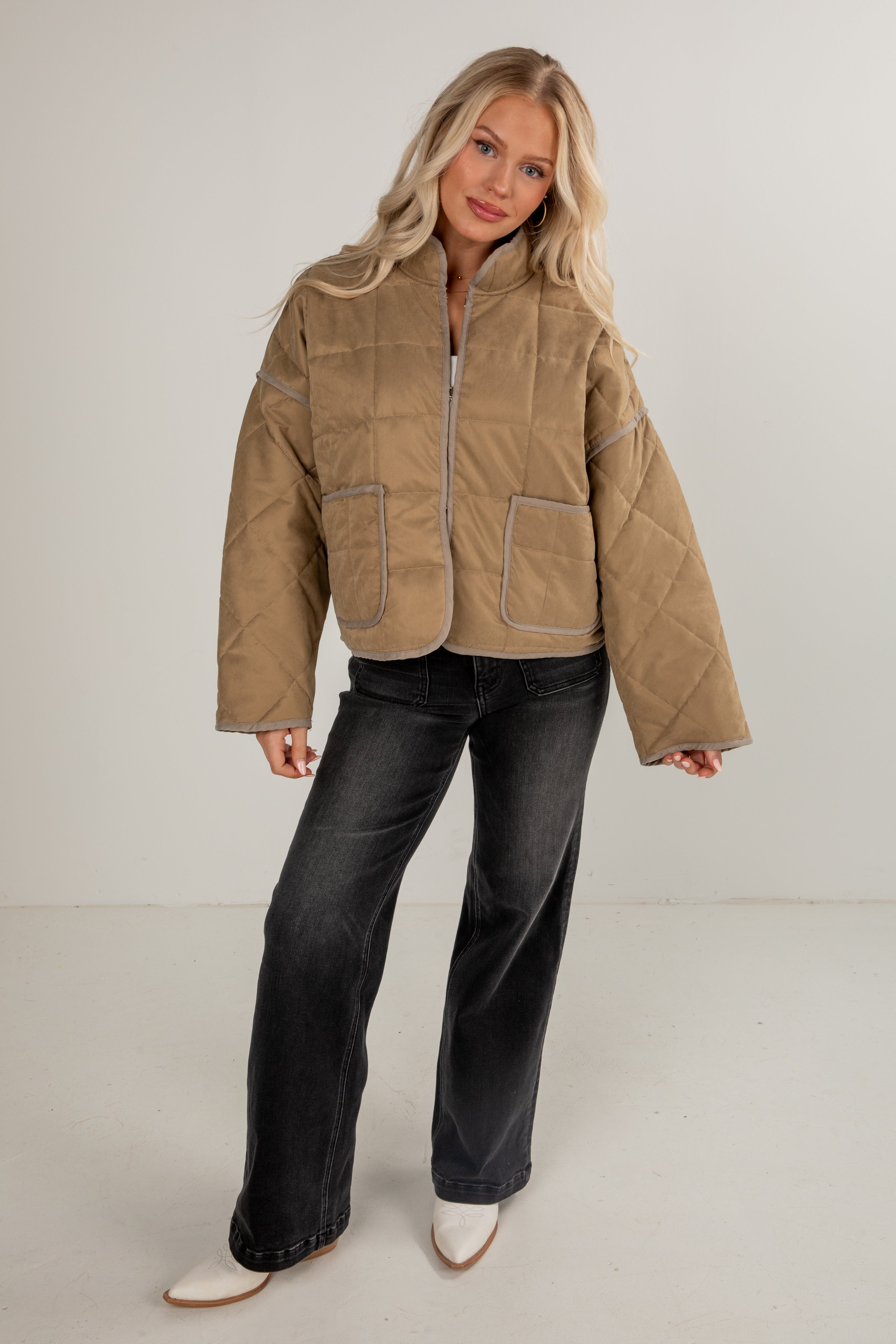 Woman wearing a beige quilted jacket and dark jeans on a plain background