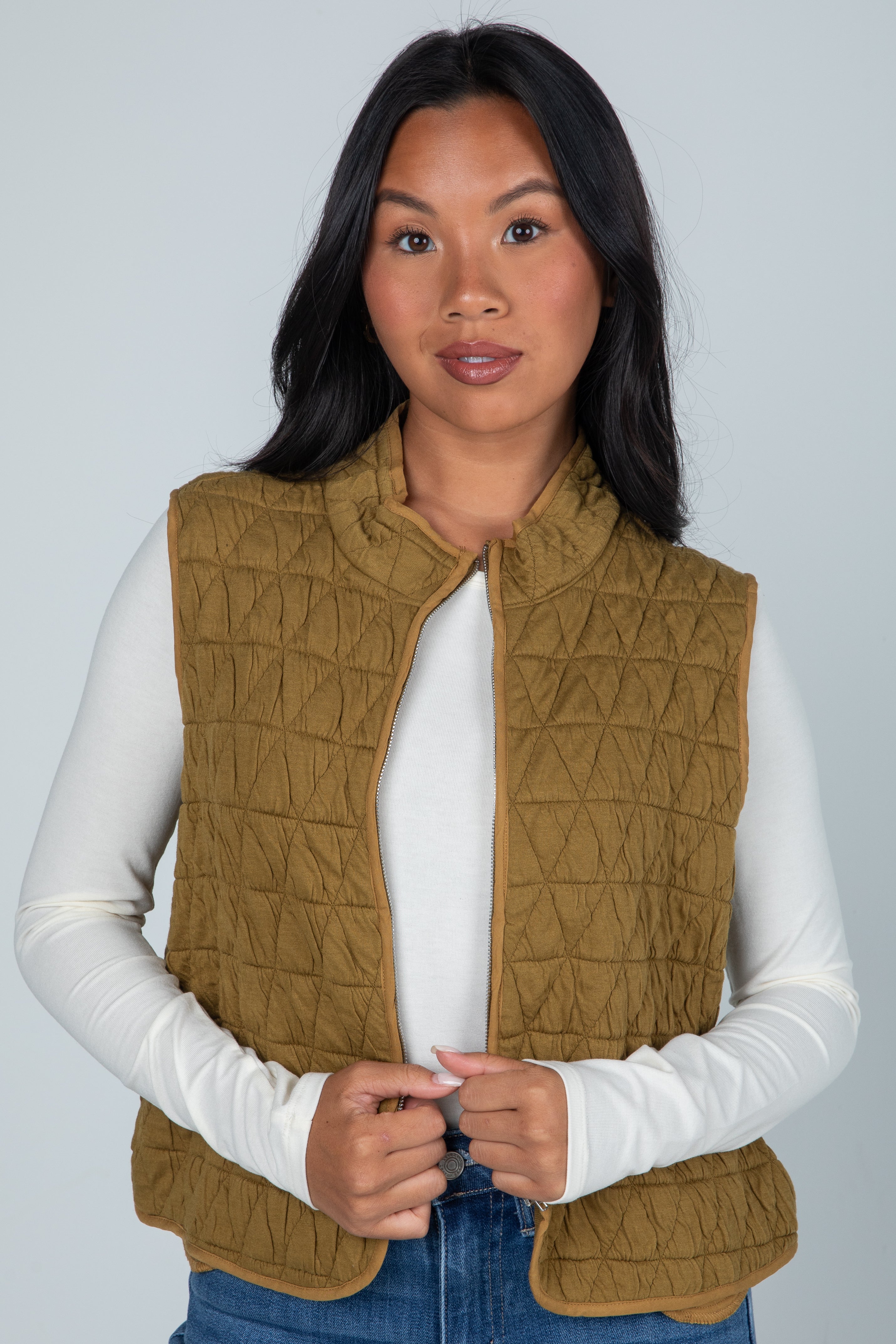 Woman wearing a quilted brown vest over a white long-sleeve shirt against a plain background