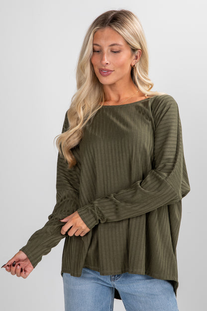 Woman wearing an olive green ribbed sweater and blue jeans on a white background