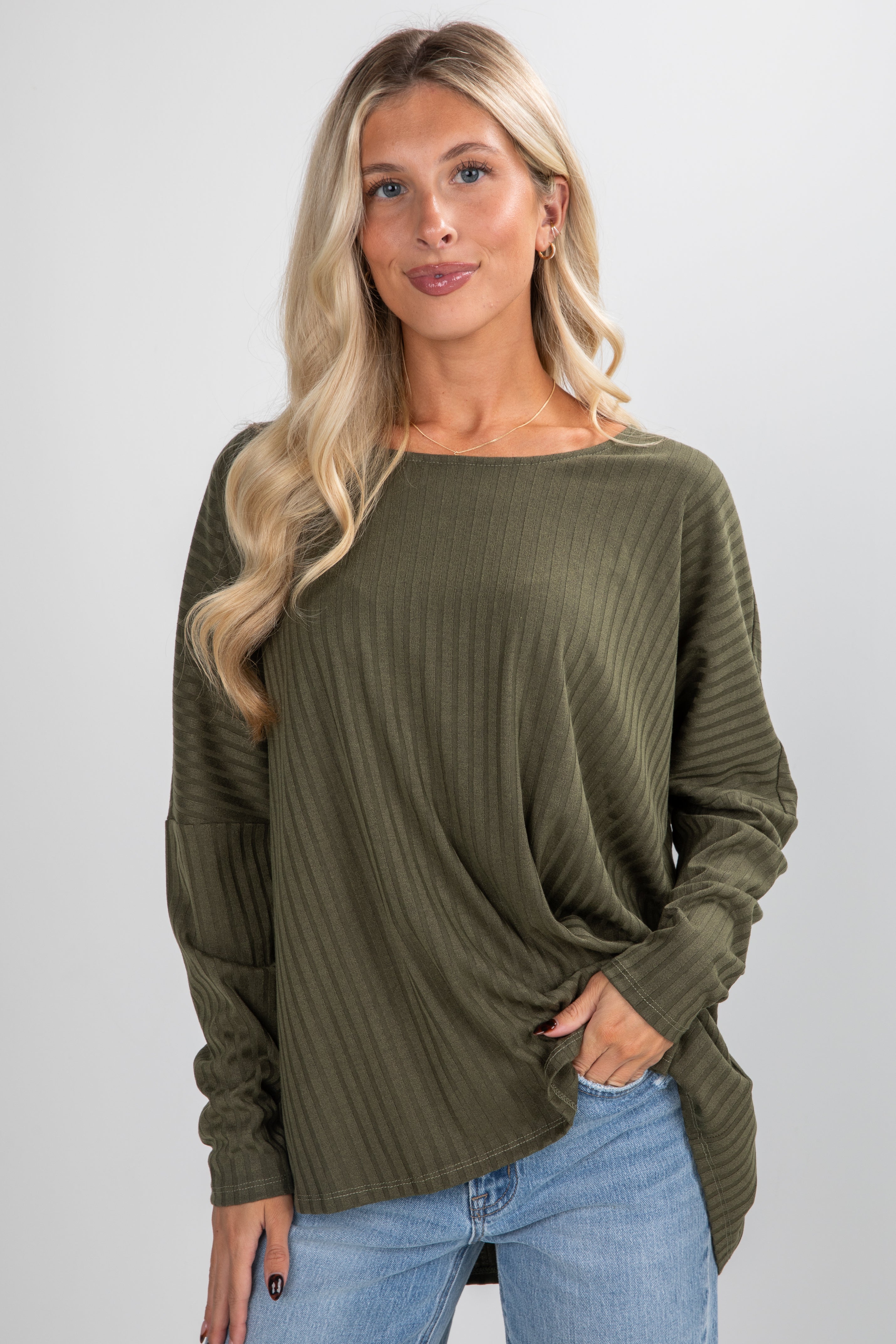 Woman wearing an olive green sweater and light blue jeans on a white background