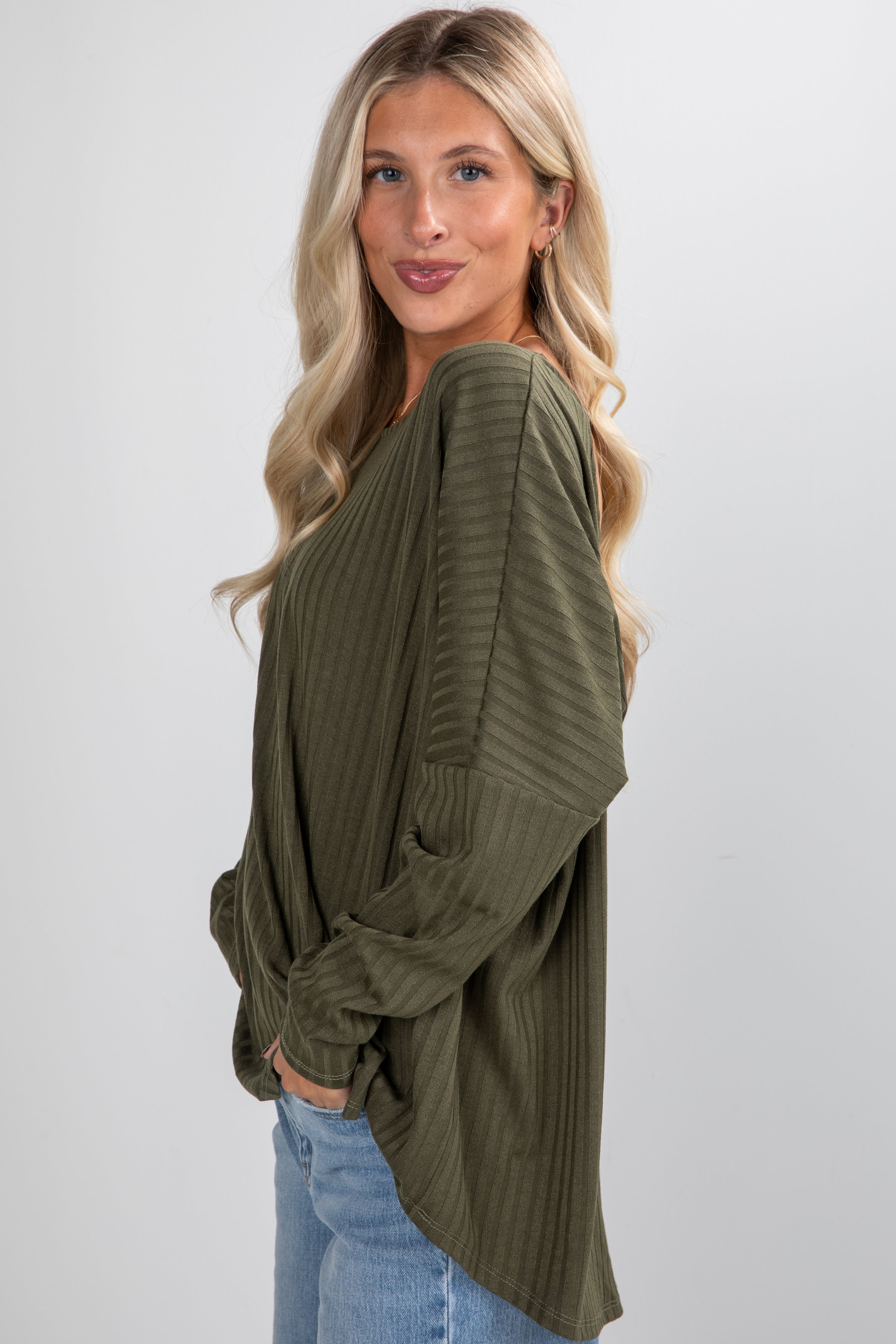 Woman wearing an olive green ribbed sweater and blue jeans on a white background