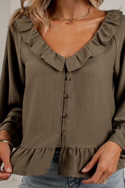 A woman wearing a long-sleeve olive brown blouse with a ruffled collar, button-front closure, and ruffled hem, paired with blue jeans.
