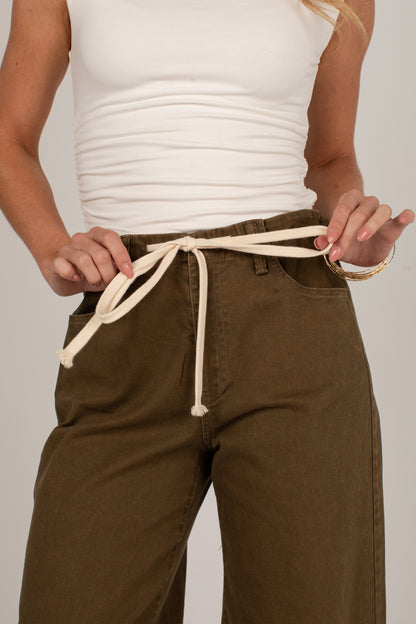 A close-up of a person wearing olive green wide-leg pants with an off-white drawstring belt tied at the waist, paired with a white ribbed tank top.