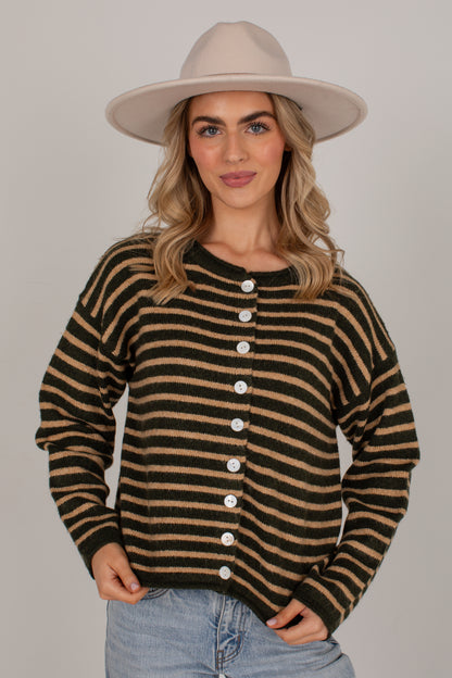 A woman wearing a beige wide-brim hat, a brown and tan striped button-up cardigan, and light blue jeans, standing against a solid light gray background.