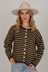 A woman wearing a beige wide-brim hat, a brown and tan striped button-up cardigan, and light blue jeans, standing against a solid light gray background.