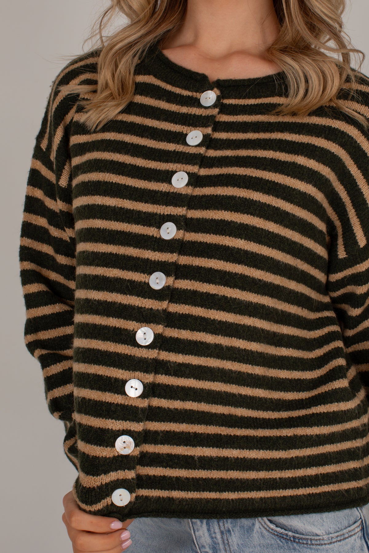A close-up of a woman wearing a fuzzy knit cardigan with horizontal black and tan stripes, featuring a button-down front with white buttons.