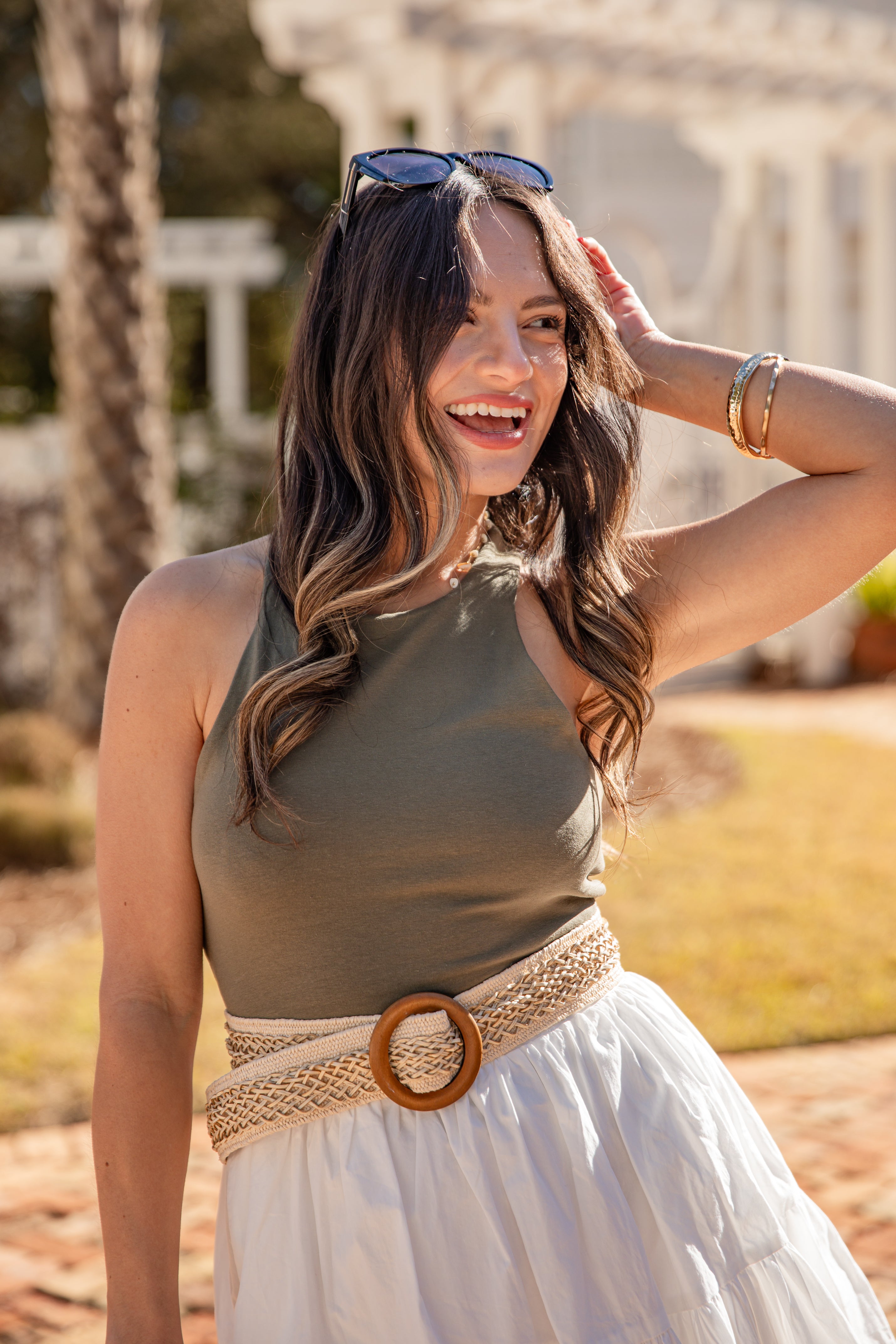 Woman in a green top and white skirt with a woven belt, standing outdoors.