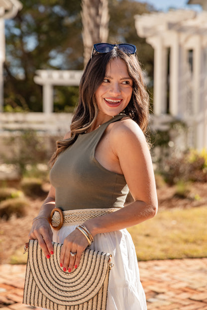 Woman holding a woven handbag in an outdoor setting with classical architecture.