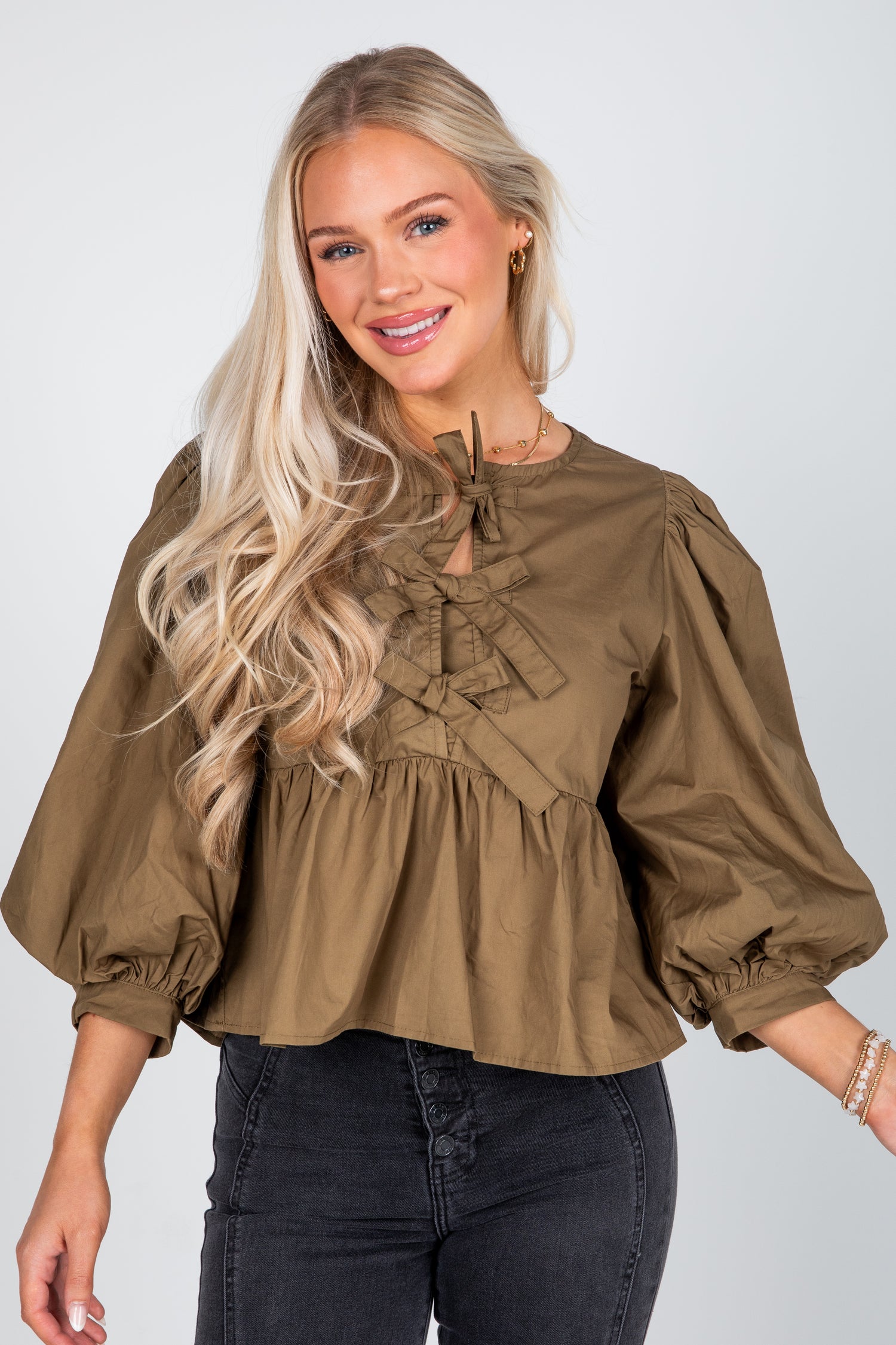 Woman wearing a brown blouse with puff sleeves on a plain background