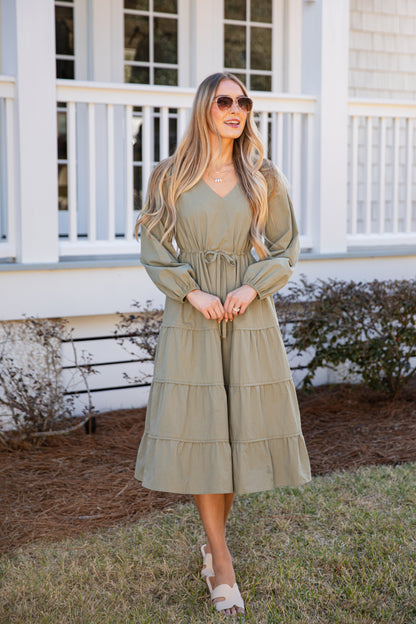 Woman wearing a green dress standing in front of a white house with a porch.