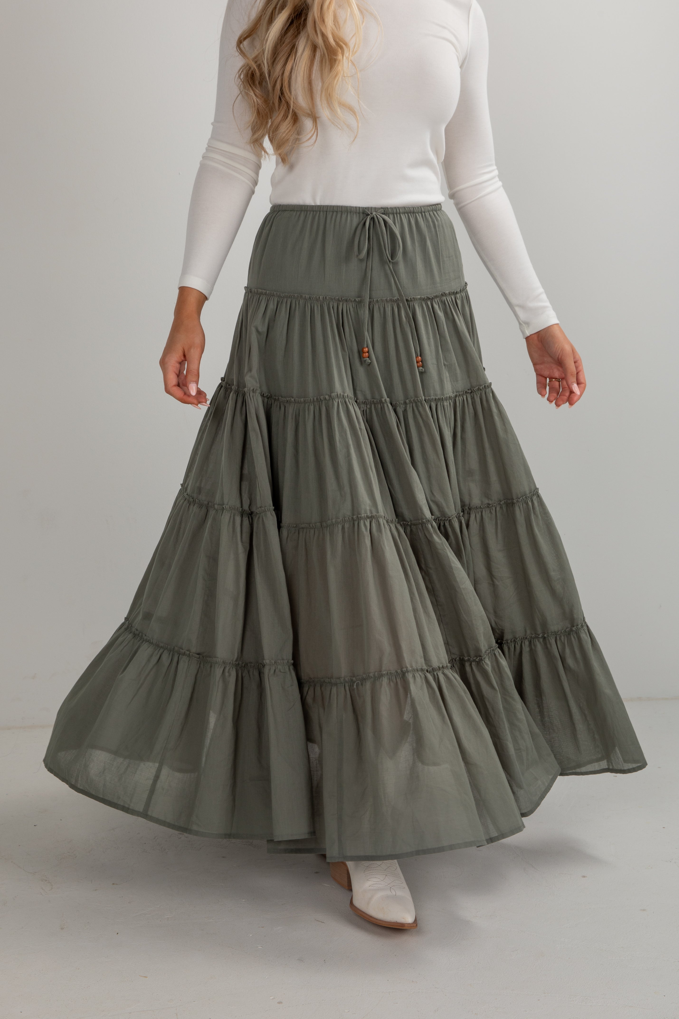 Woman wearing a long, tiered green skirt against a plain background