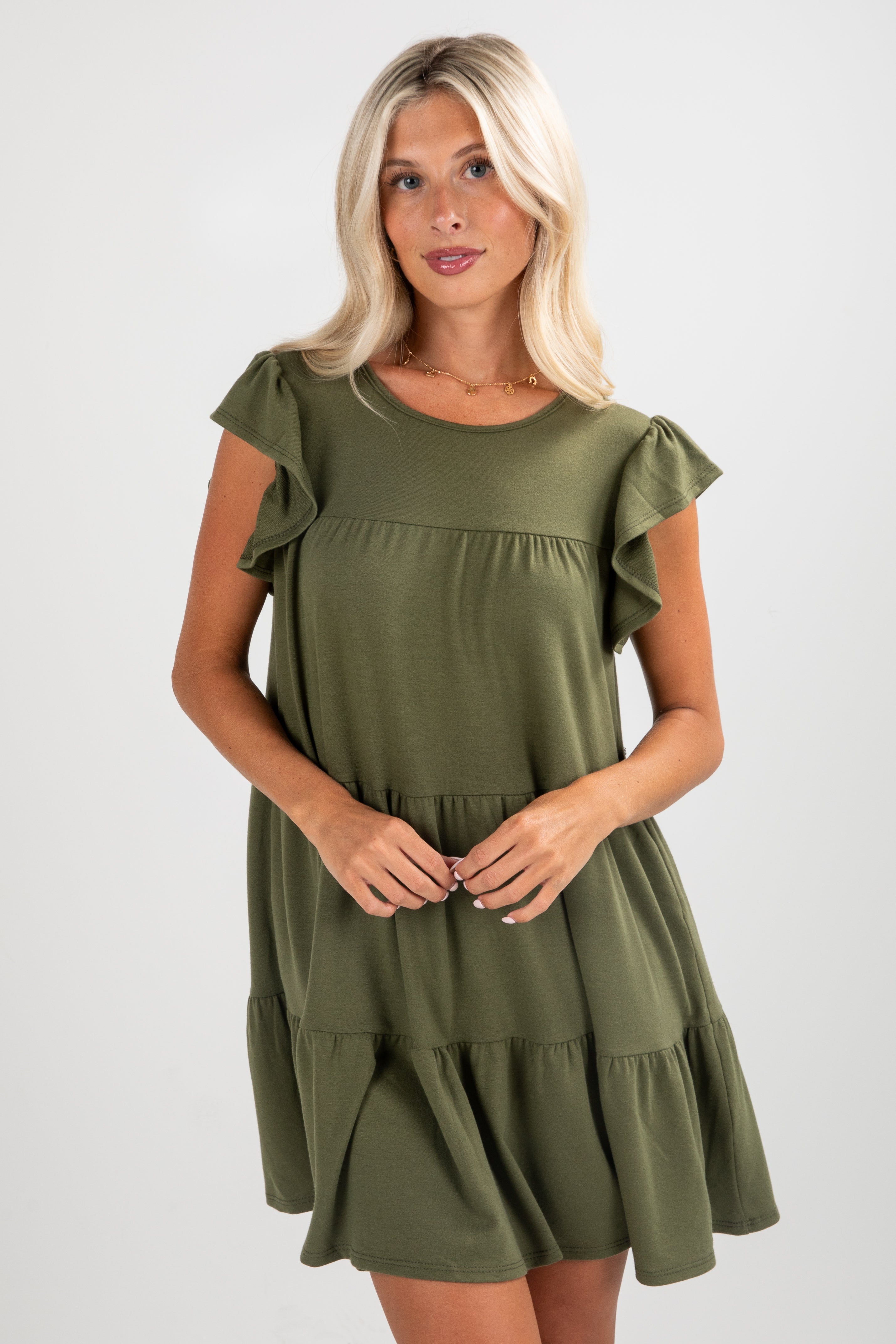 Woman wearing an olive green dress with ruffled sleeves on a white background