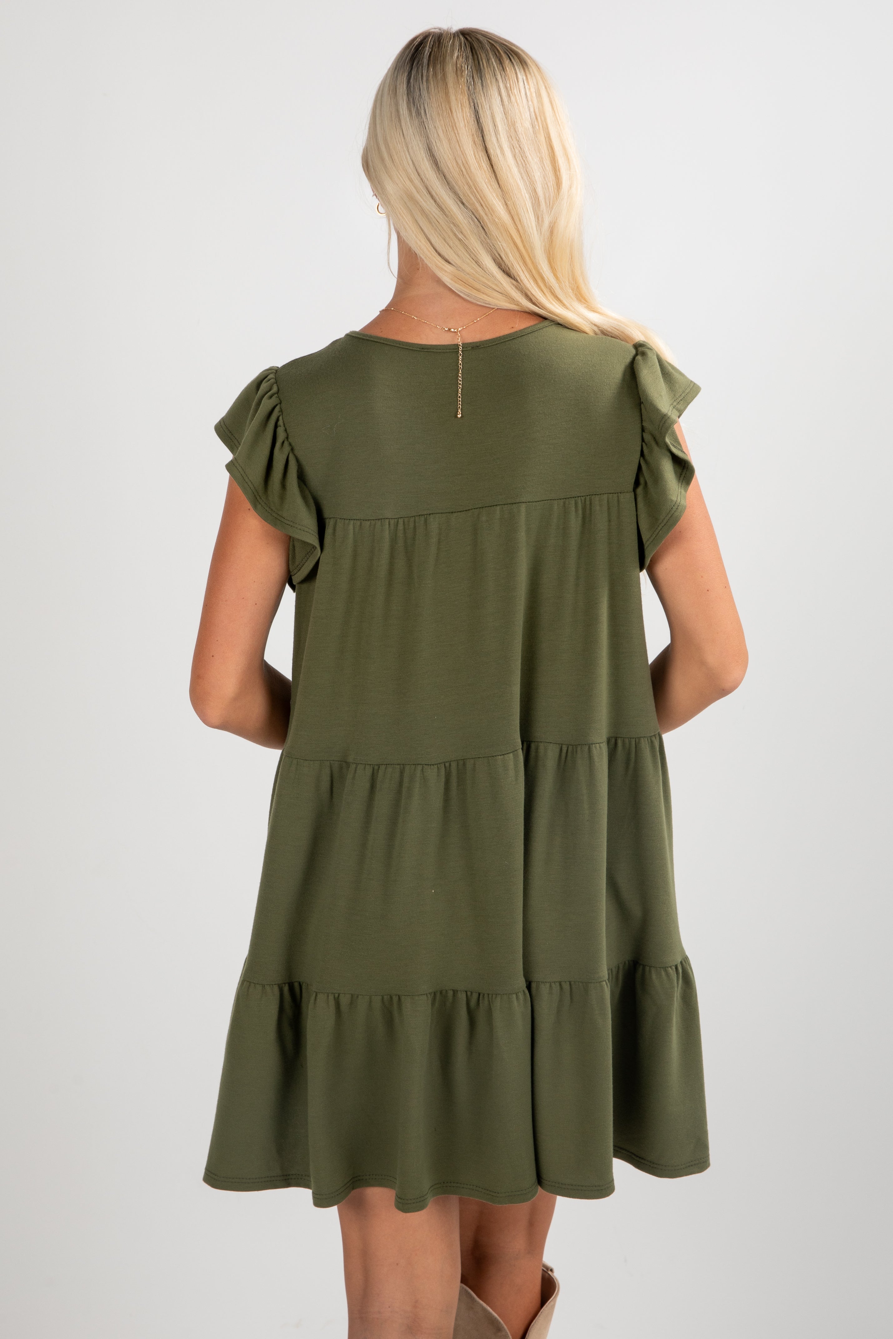 Woman wearing an olive green dress with ruffled sleeves on a white background