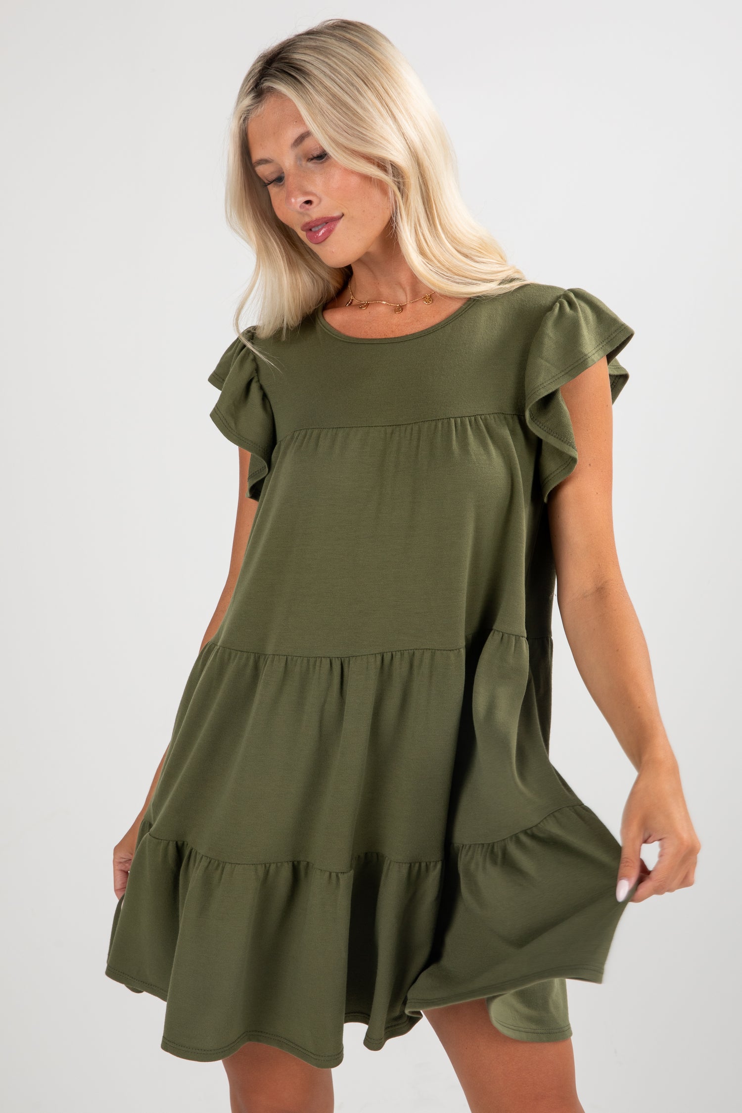 Woman wearing an olive green dress with ruffled sleeves and bottom hem on a white background